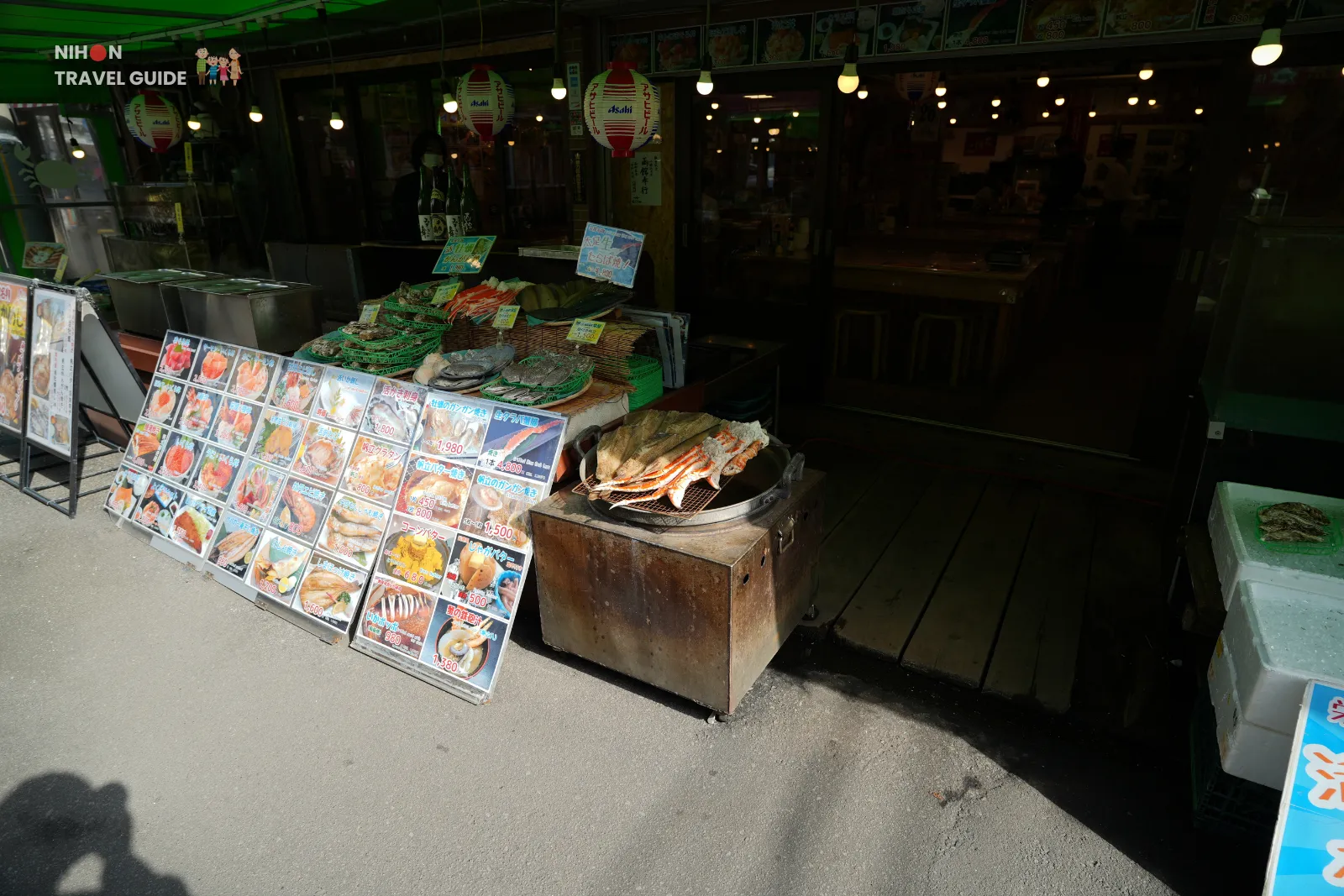 Exterior of a Hakodate Morning Market restaurant with photo menus and grilled crab legs cooking at the entrance.