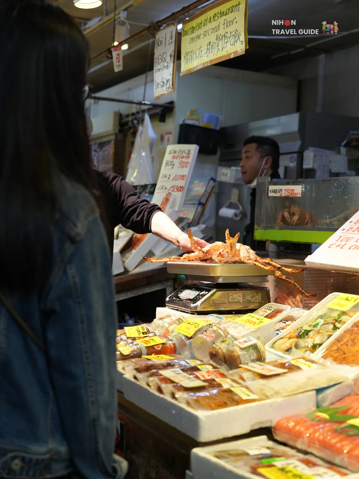 Seafood vendor standing behind trays of fish and fillets at Hakodate Morning Market.