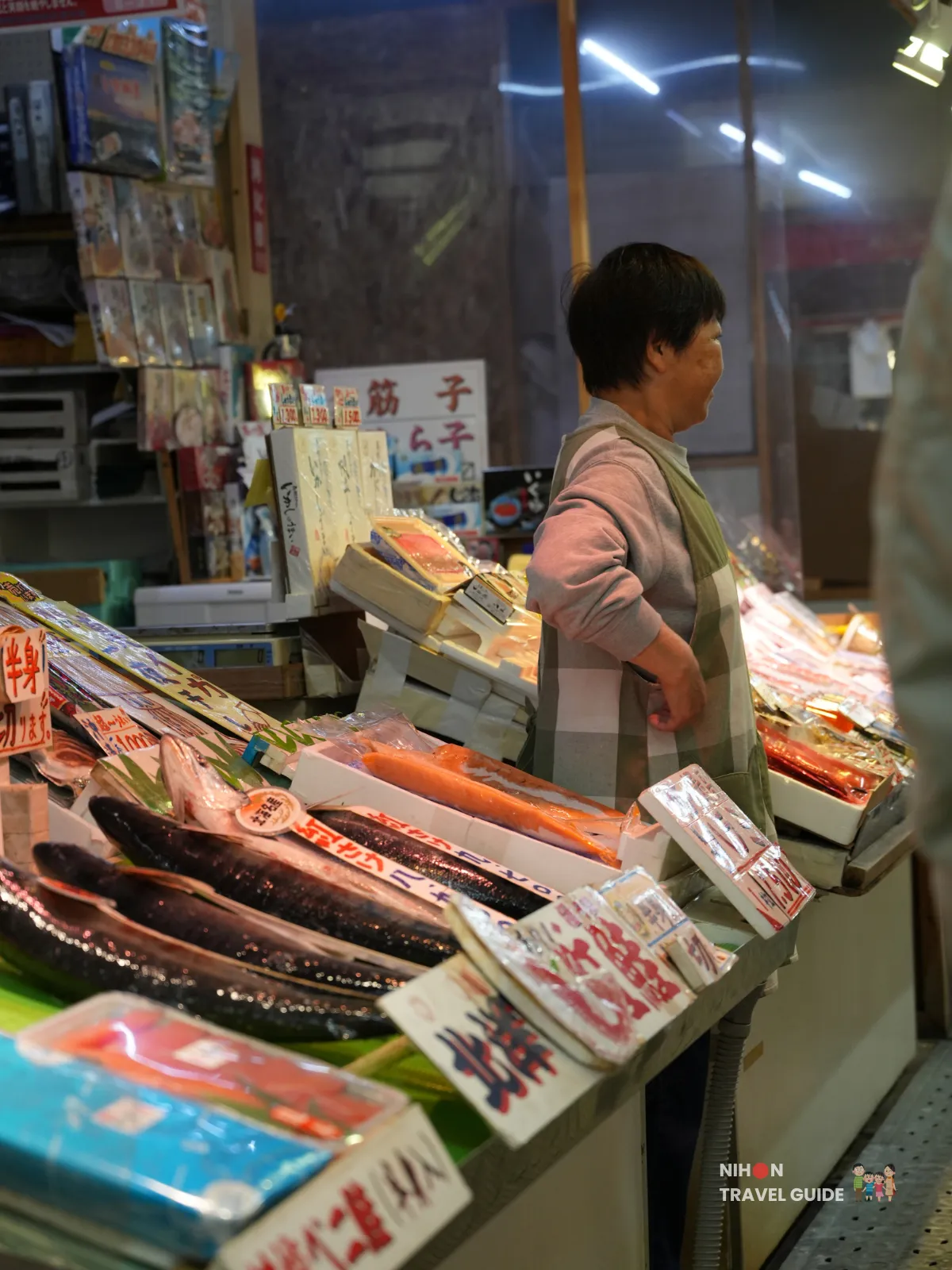 Seafood vendor standing behind trays of fish and fillets at Hakodate Morning Market.