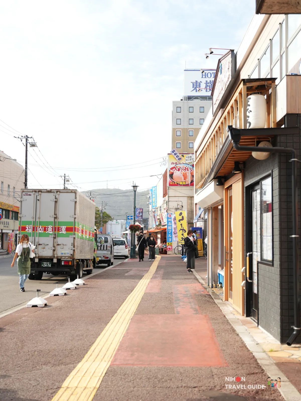 Street leading to Hakodate Morning Market lined with shops, signs, and pedestrians in Hokkaido.
