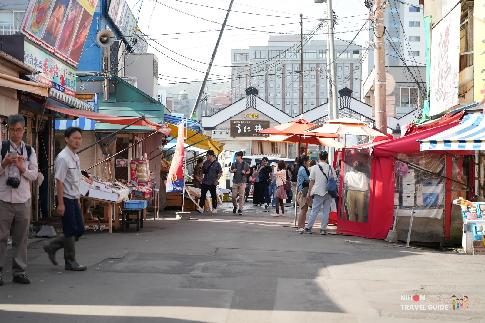 People walking through an outdoor street lined with food stalls and colorful tents at Hakodate Morning Market in Hokkaido, Japan.