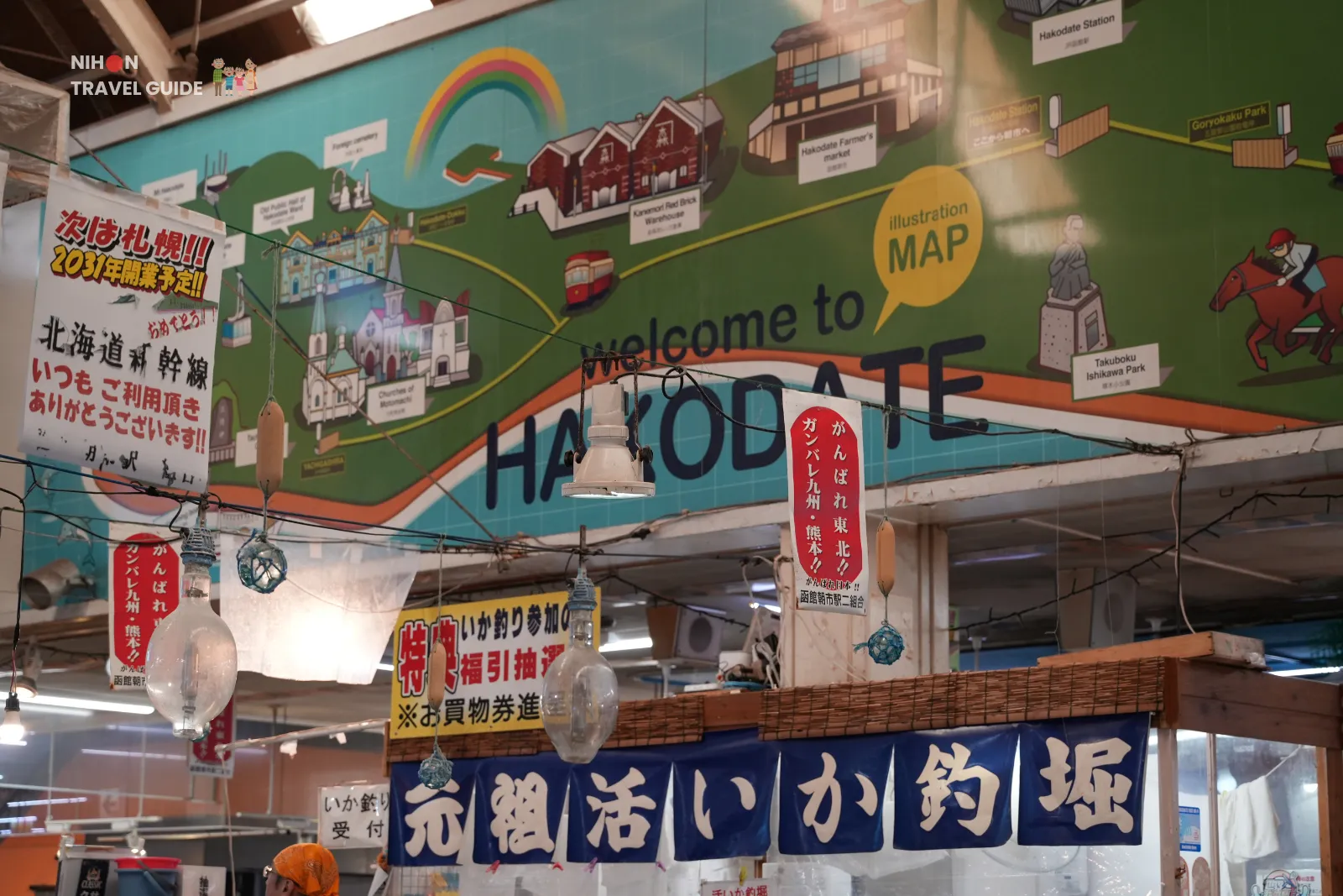 Illustrated welcome to Hakodate map sign hanging above stalls inside Hakodate Morning Market.