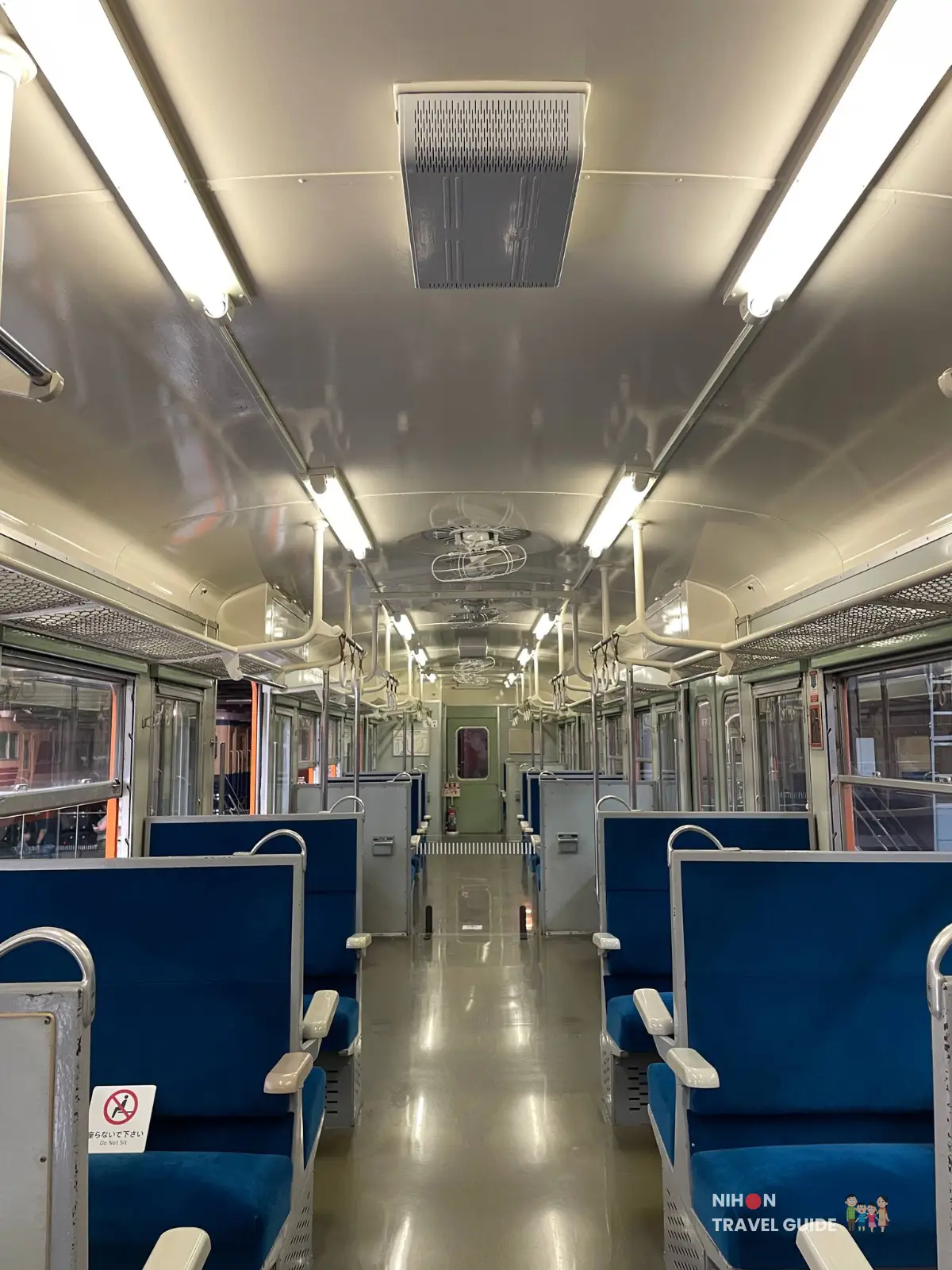 Interior of a classic Japanese electric train car with blue bench seats, metal handrails, and fluorescent lighting at SCMaglev and Railway Park.