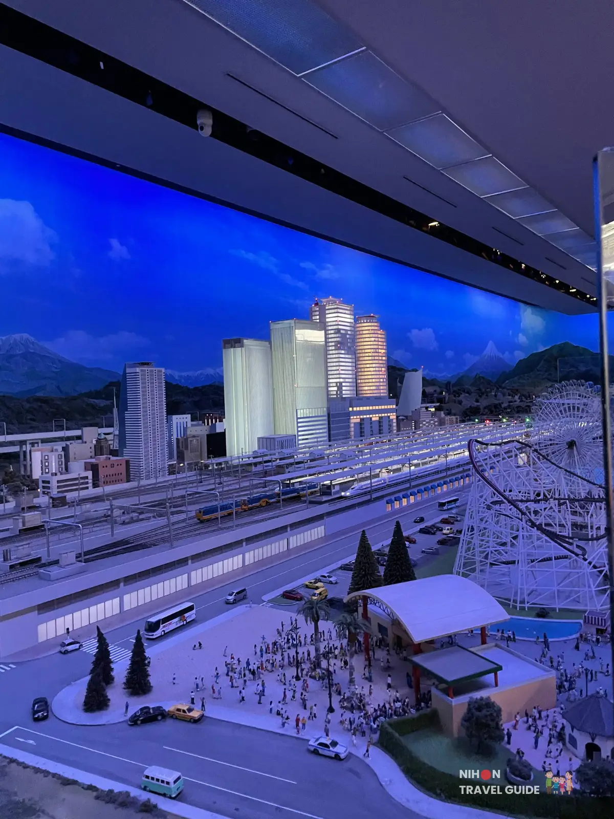 City and station diorama at SCMaglev and Railway Park with glowing towers, Shinkansen tracks, an amusement park area, and a plaza filled with miniature visitors.
