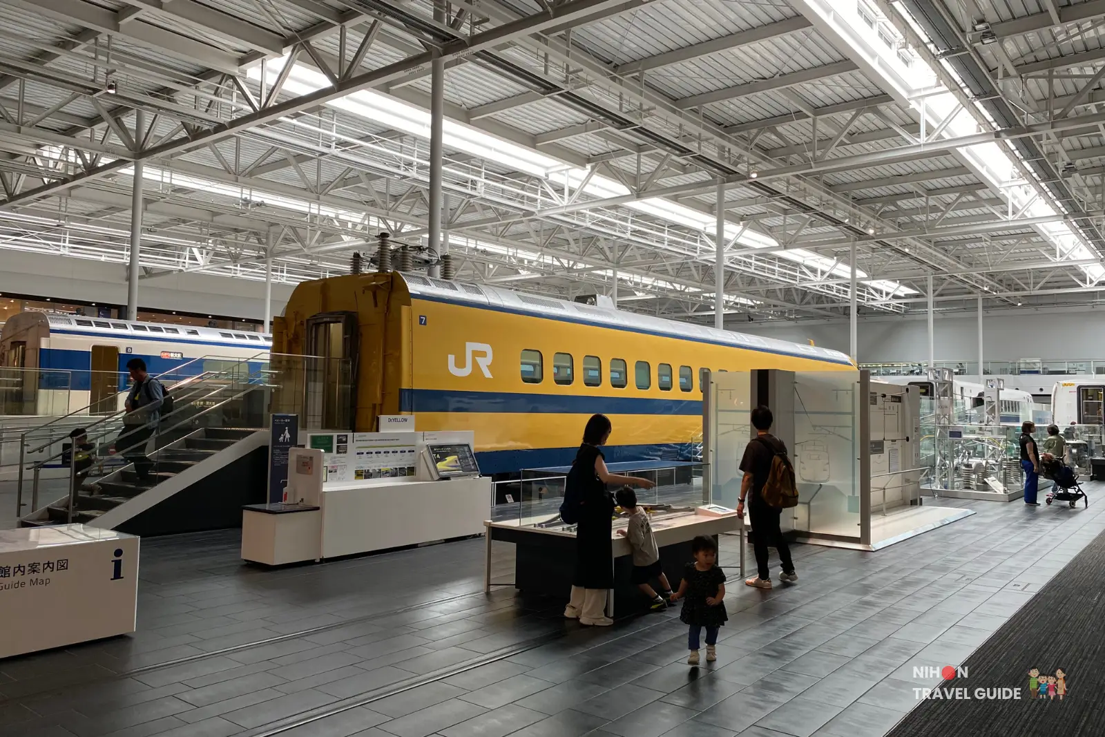 Dr. Yellow Shinkansen carriage displayed indoors with information panels and families exploring the surrounding exhibits at SCMaglev and Railway Park.