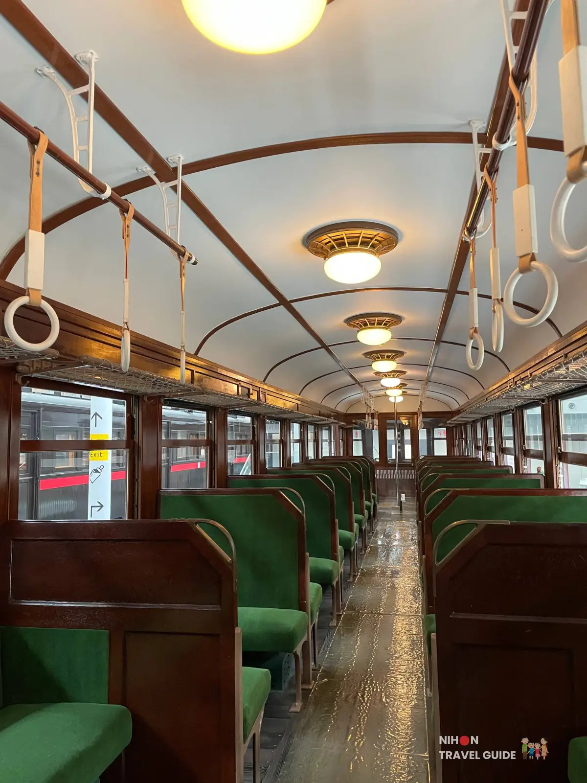 Interior of a historic wooden railway carriage with green upholstered seats, overhead straps, and warm ceiling lights at SCMaglev and Railway Park.