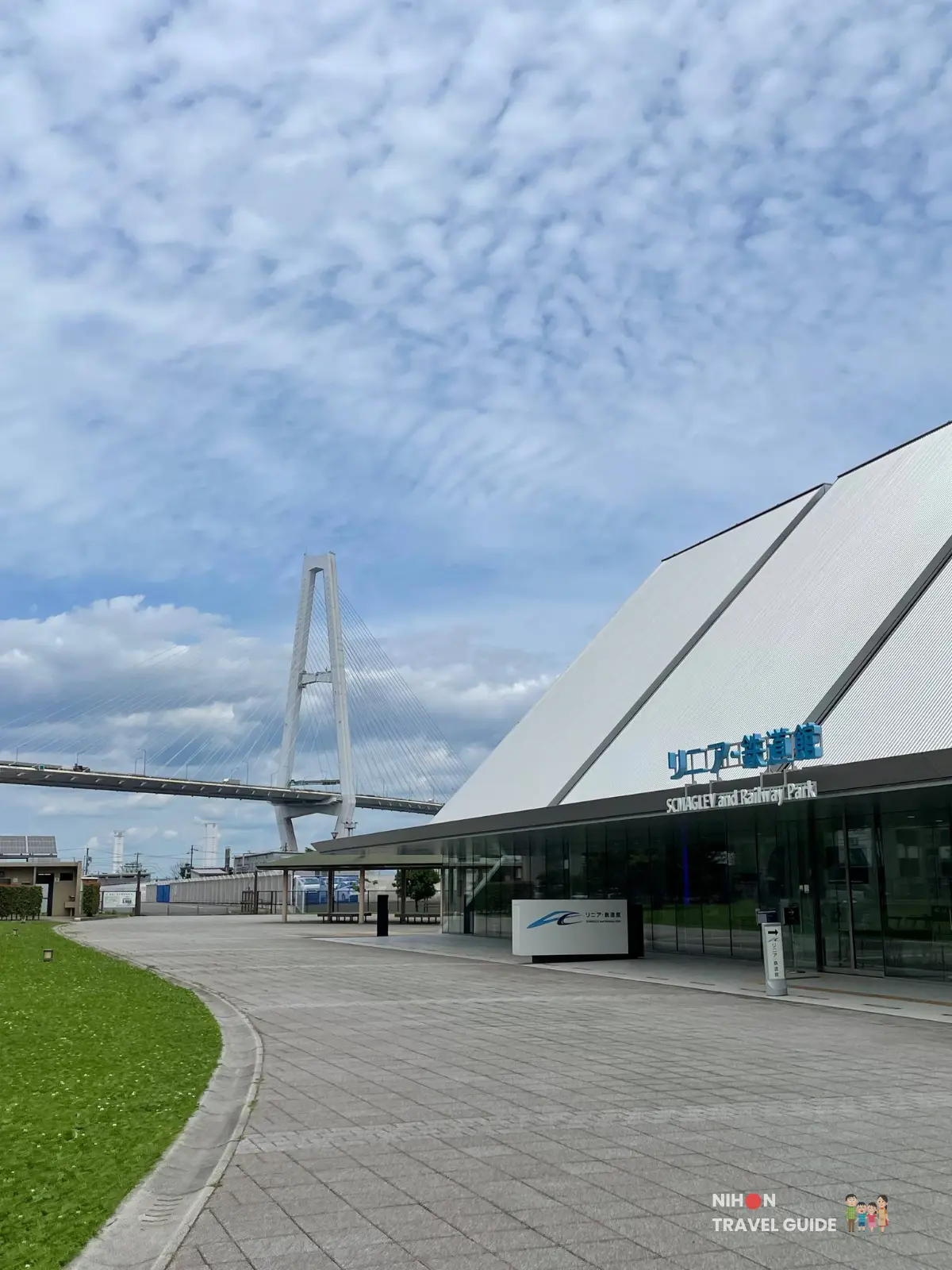 Exterior view of SCMaglev and Railway Park in Nagoya with its white angular roof and a large cable-stayed bridge in the background under a bright sky.