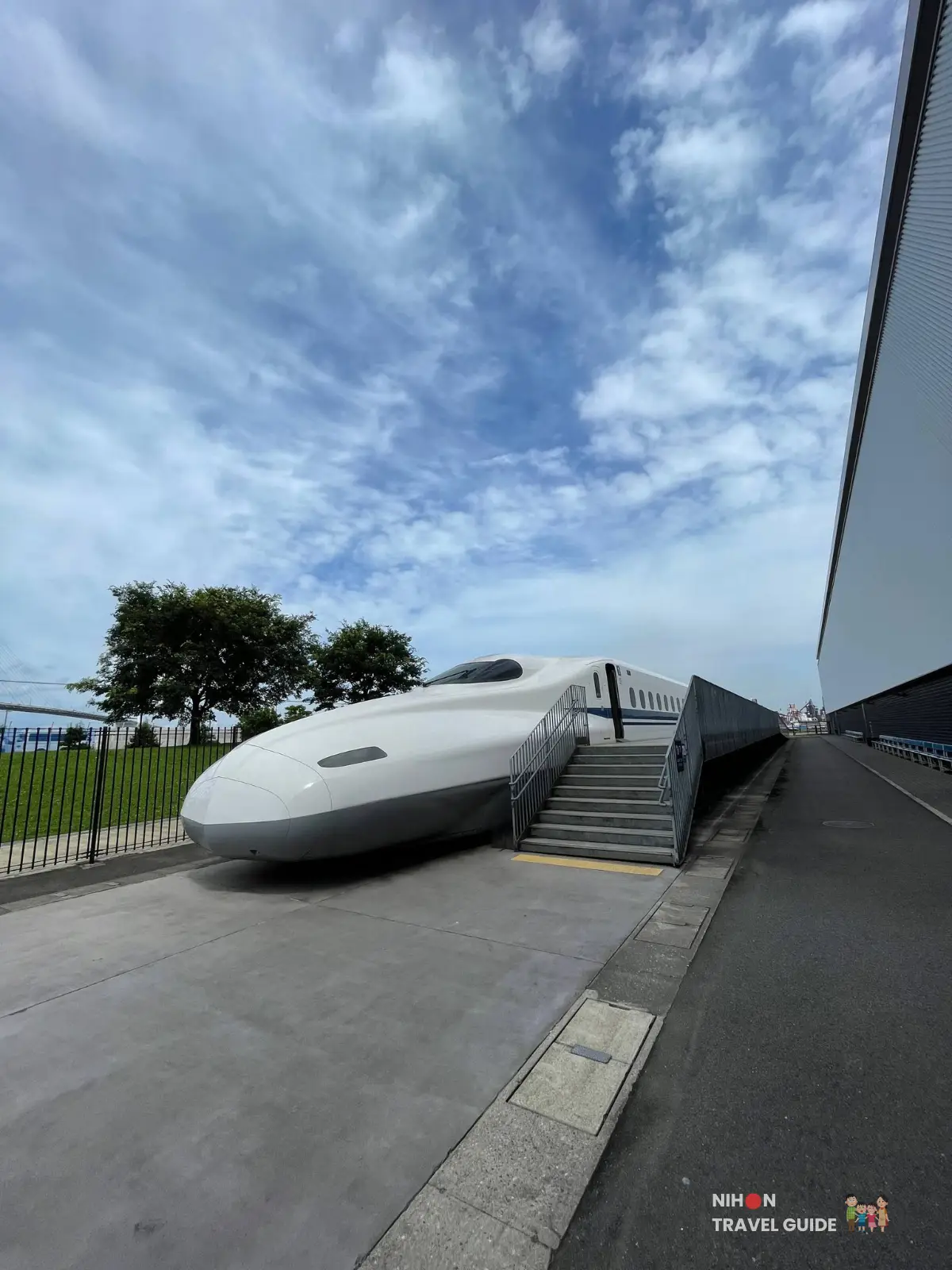 Outdoor N700 Shinkansen car at SCMaglev and Railway Park with visitor stairs beside it under a bright blue sky.
