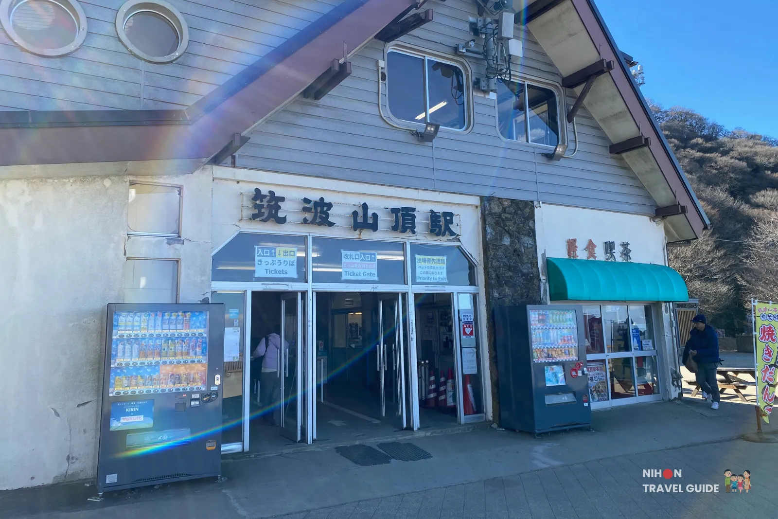 cable-car-station-mt-tsukuba-summit-village Exterior of the Mount Tsukuba summit village cable car station, with ticket entrances, Japanese signage, and drink vending machines under a clear blue sky.