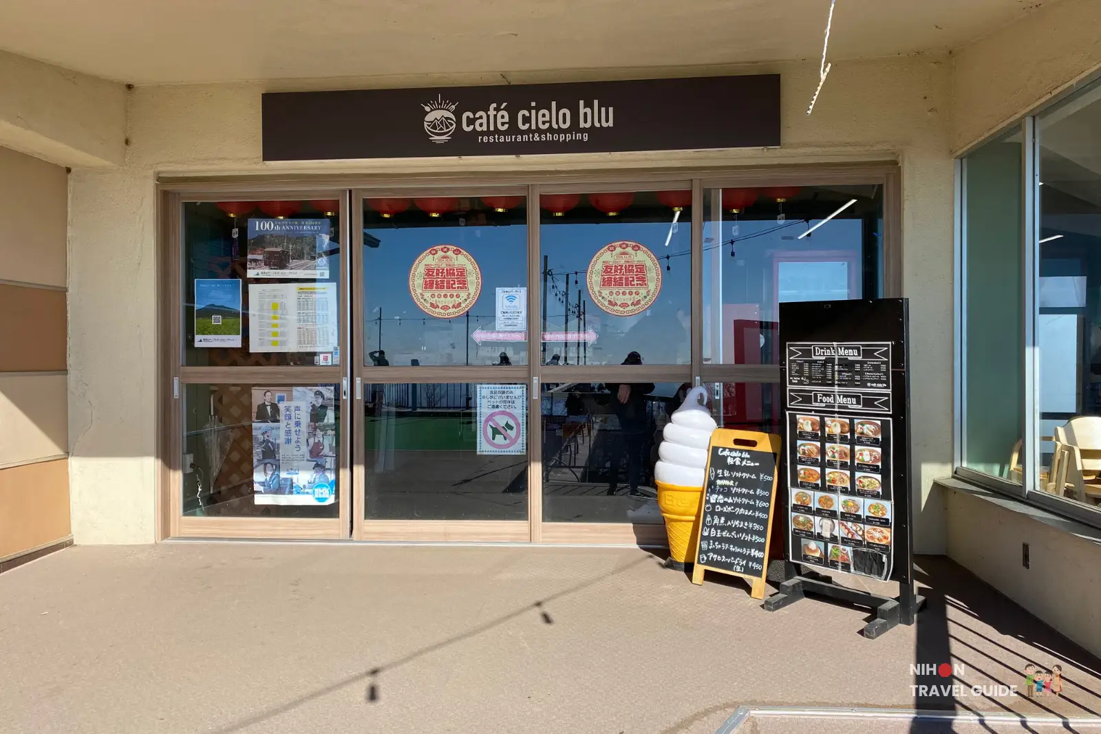 mt-tsukuba-cafe-cielo-blu-entrance Front entrance of Café Cielo Blu on Mount Tsukuba, showing glass doors with posters and lanterns, plus outdoor menu boards and a large soft-serve cone display by the doorway.