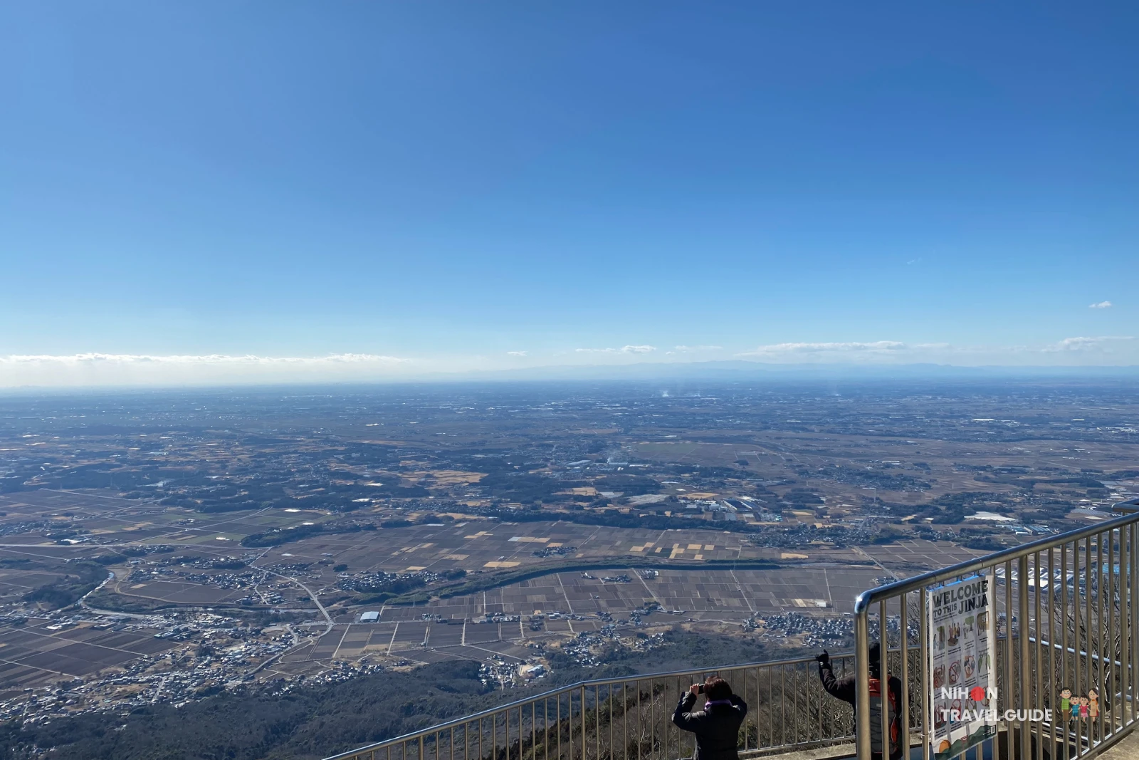 Elevated view from Nantaisan Peak overlooking valley forests, towns, and grid-like fields under a bright blue winter sky.