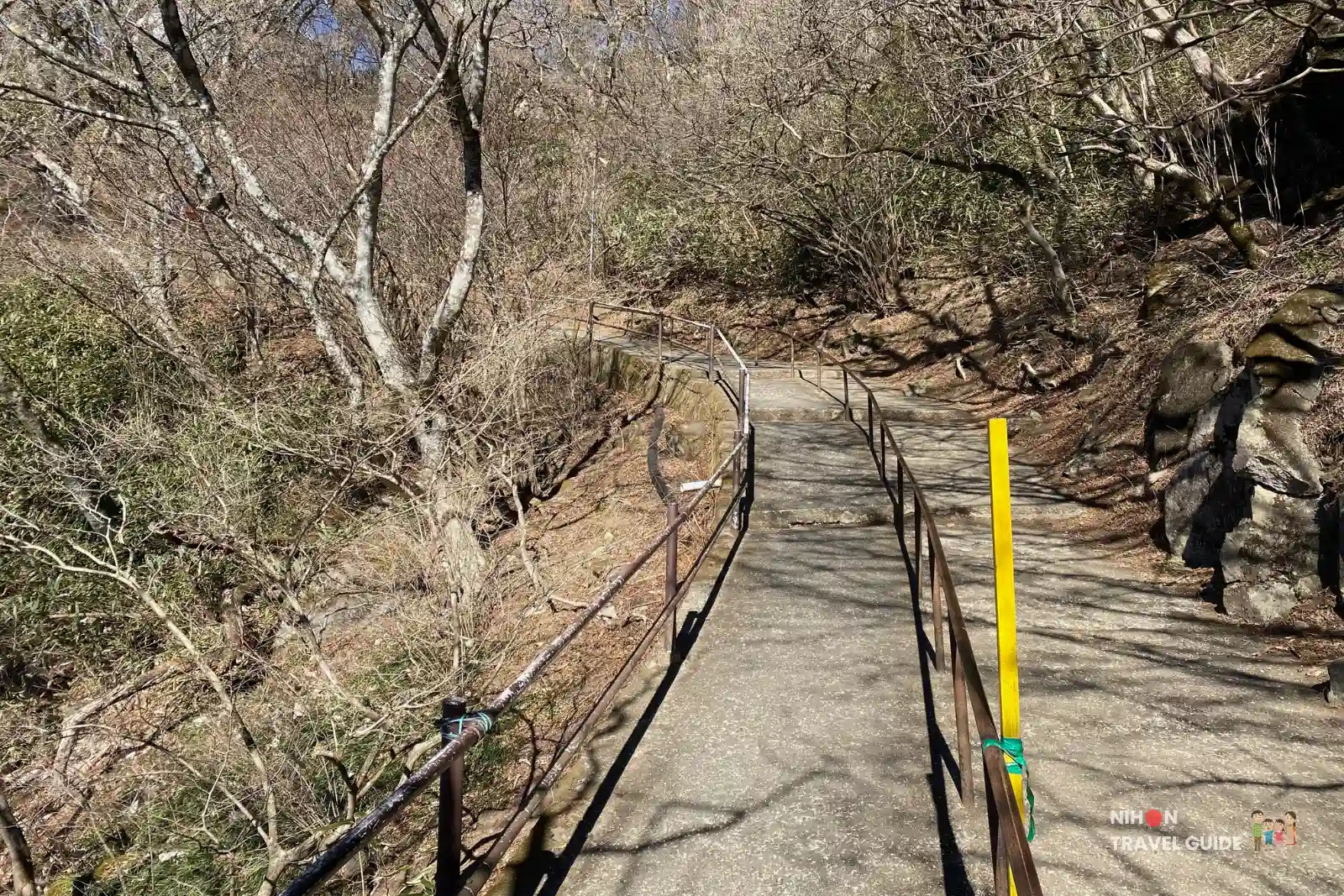 mt-tsukuba-nyotaisan-trail-from-ropeway-summit Paved path with handrails leading uphill through bare winter trees from the Mount Tsukuba ropeway summit station toward the Nyotaisan Peak hiking trail.