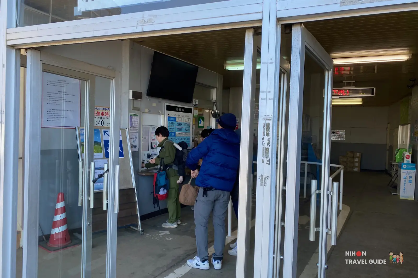 mt-tsukuba-summit-cable-car-station-entrance Hikers lining up at the ticket counter just inside the glass entrance of the Mount Tsukuba summit cable car station, with fare boards and notices visible on the interior wall.