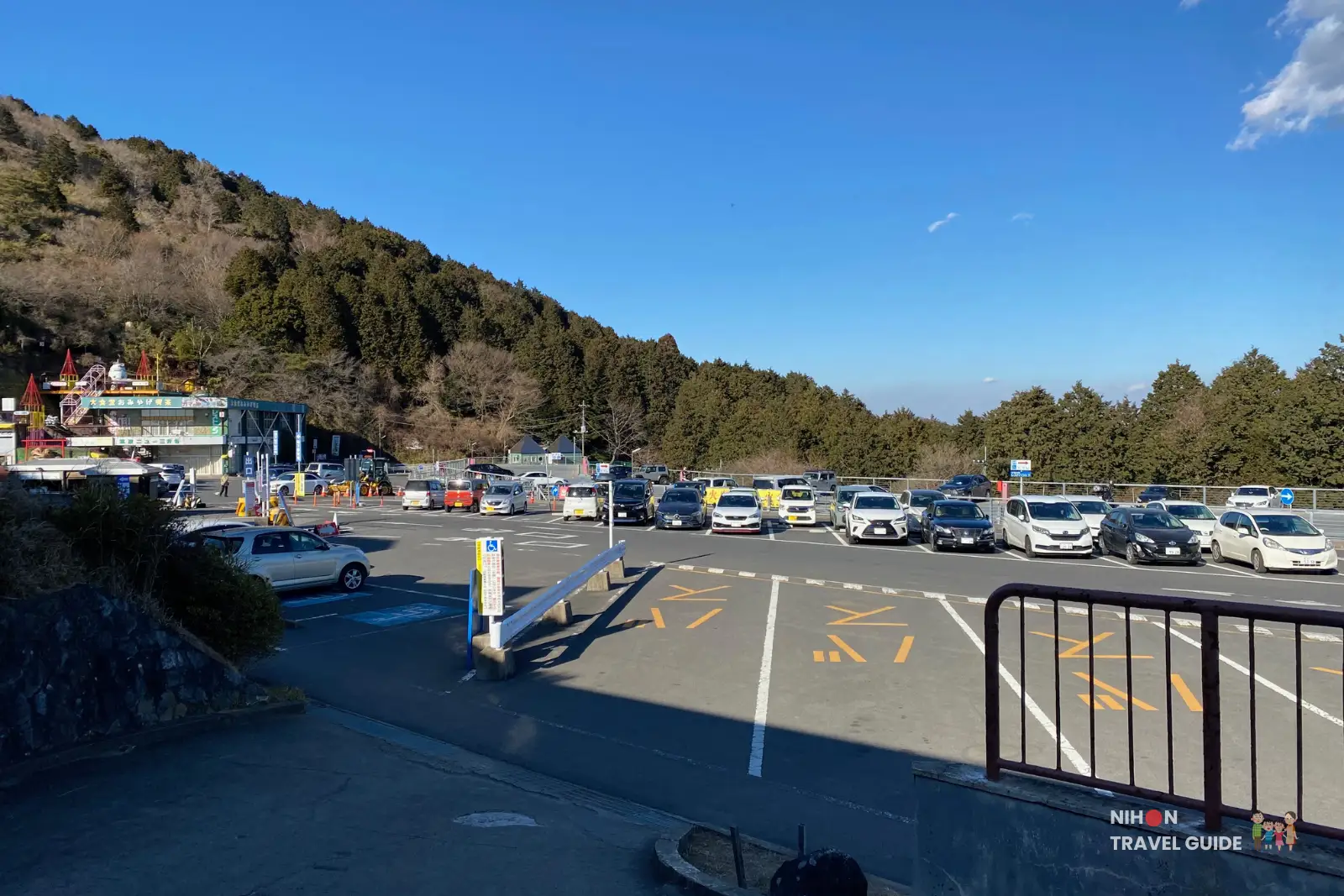 mt-tsukuba-tsutsujigaoka-ropeway-car-park Large car park at Tsutsujigaoka Ropeway base station on Mount Tsukuba, with many parked cars and forested slopes under a clear blue sky.