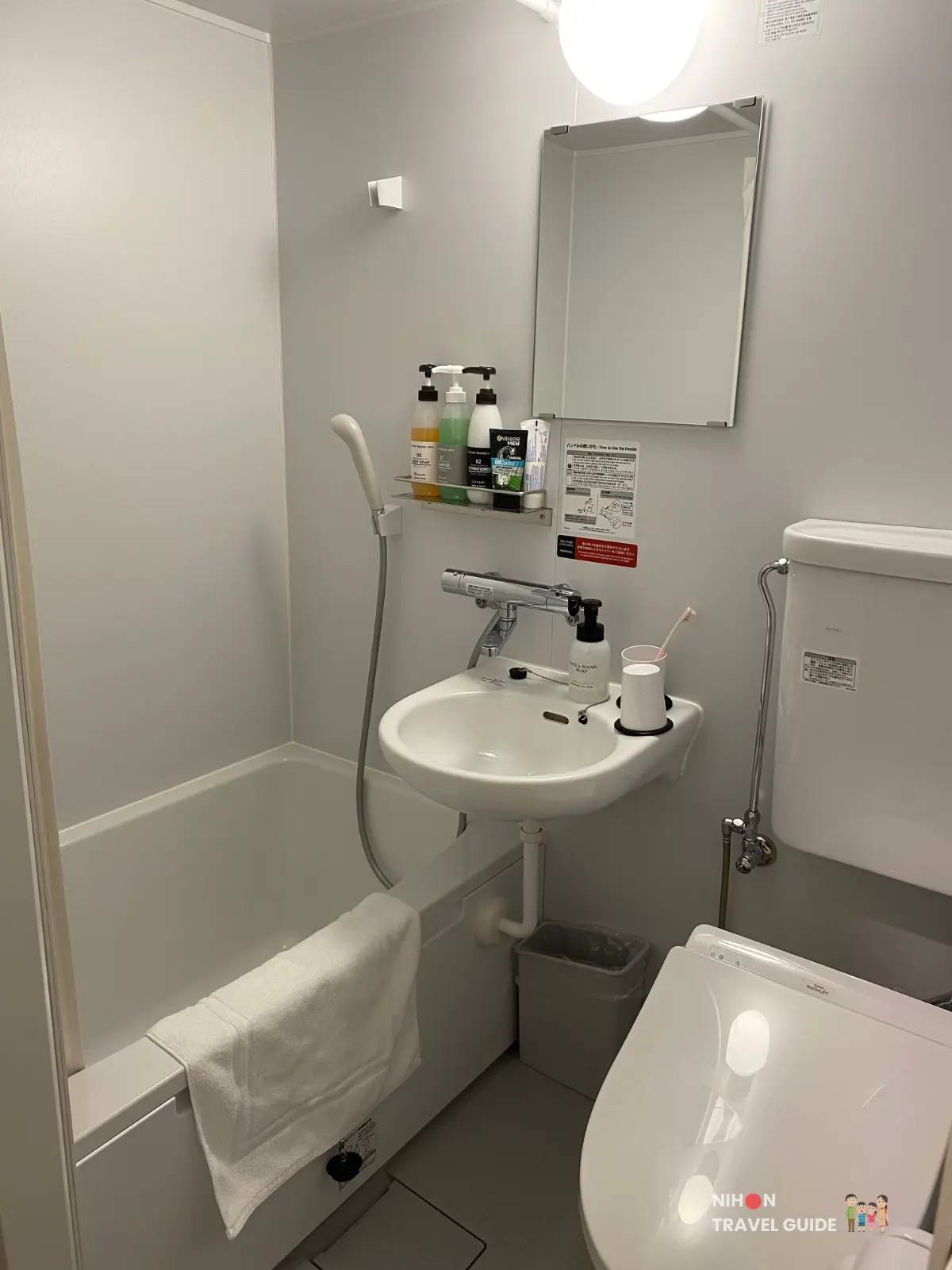 Overall view of Hotel R9 The Yard Tsukuba bathroom showing bathtub, sink, mirror, and Japanese toilet in a compact layout.