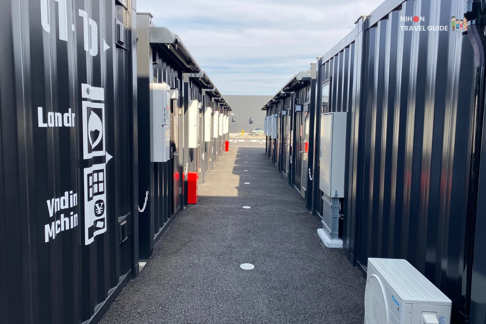 Row of black shipping-container rooms at Hotel R9 The Yard Tsukuba forming a long corridor.