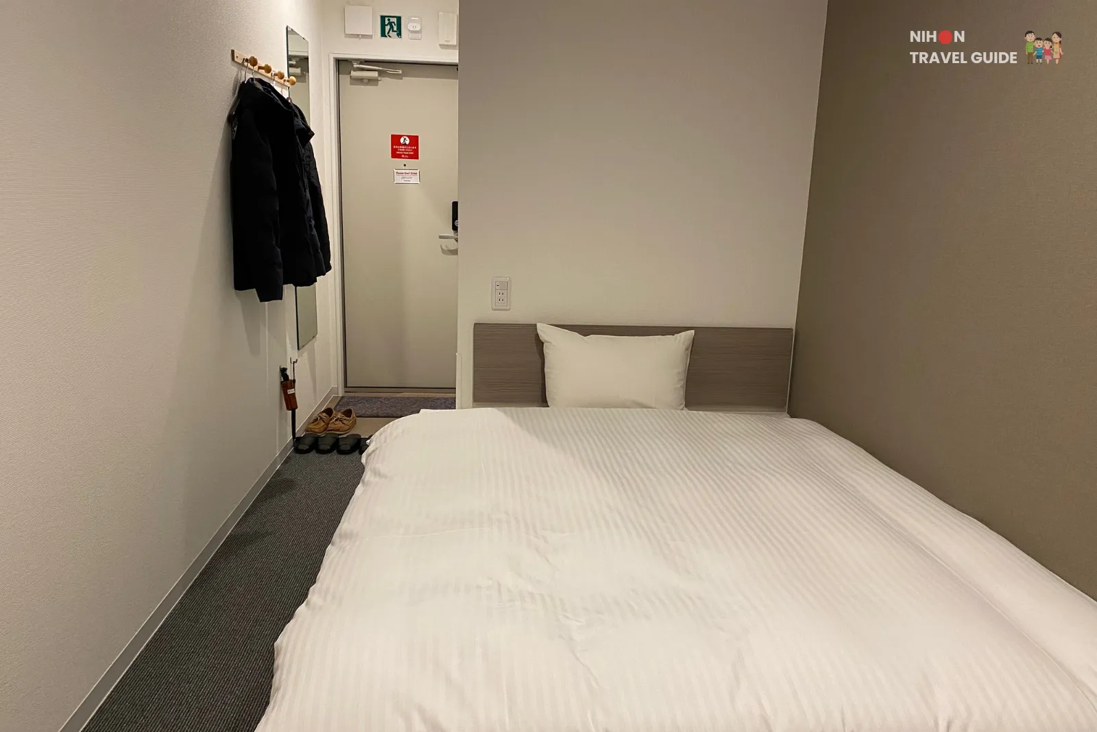 Double bed in Hotel R9 The Yard Tsukuba room with simple headboard, wall mirror, and coats hanging near the door.