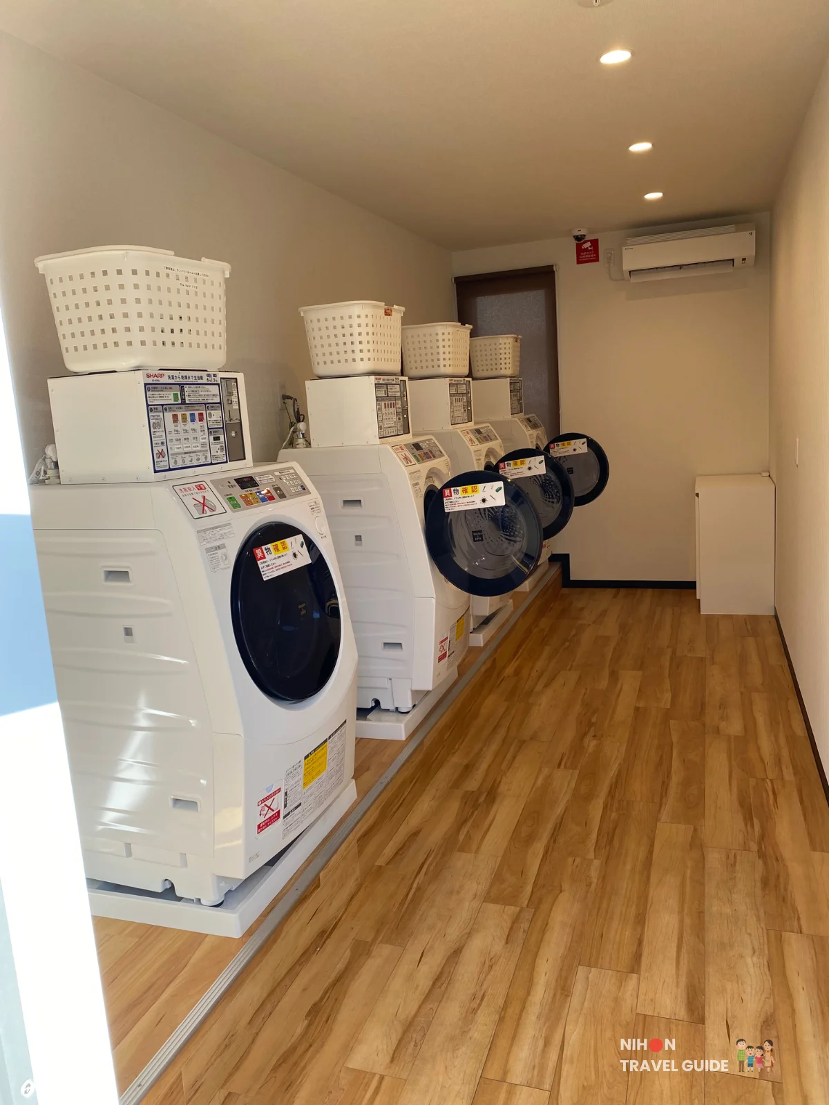 Hotel R9 The Yard Tsukuba laundry room with four coin-operated washer-dryer machines and laundry baskets.