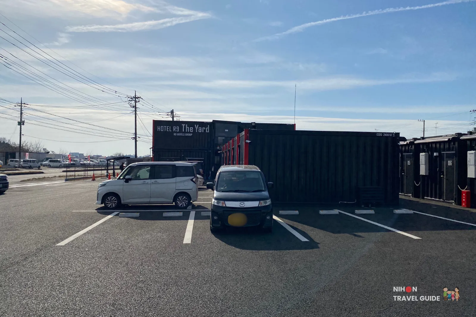 Wide shot of Hotel R9 The Yard Tsukuba exterior with container rooms and open parking area under blue sky.