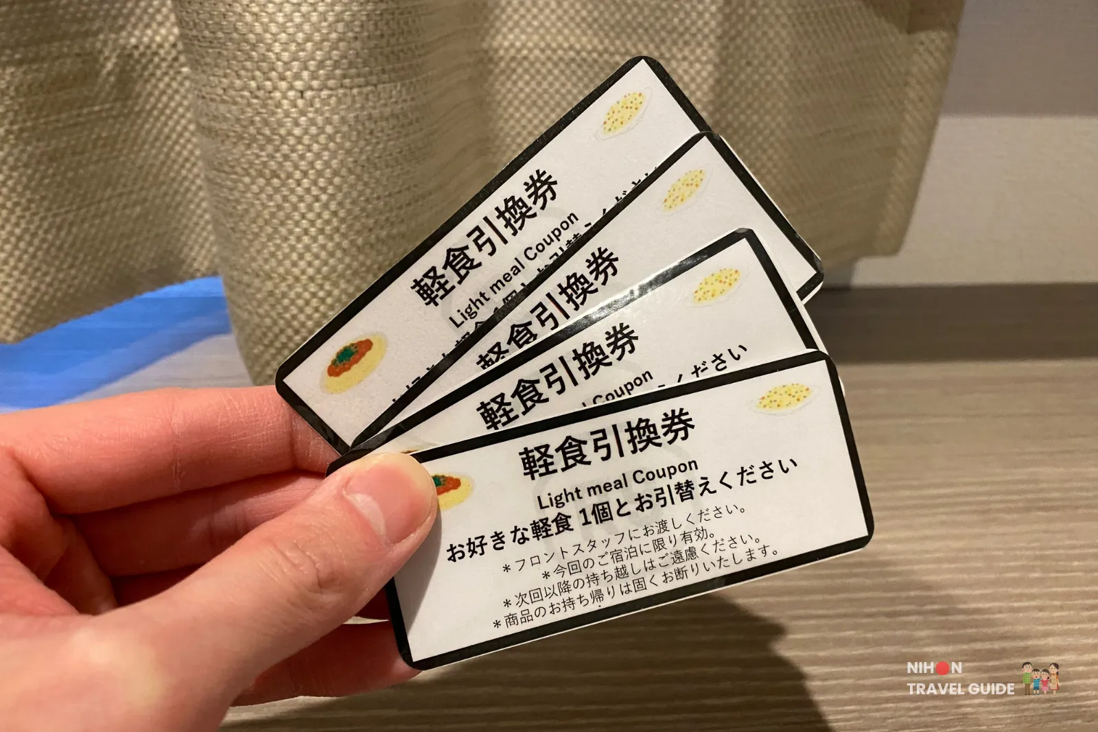 Hand holding several Hotel R9 The Yard Tsukuba light meal coupons for redeeming frozen bento meals.