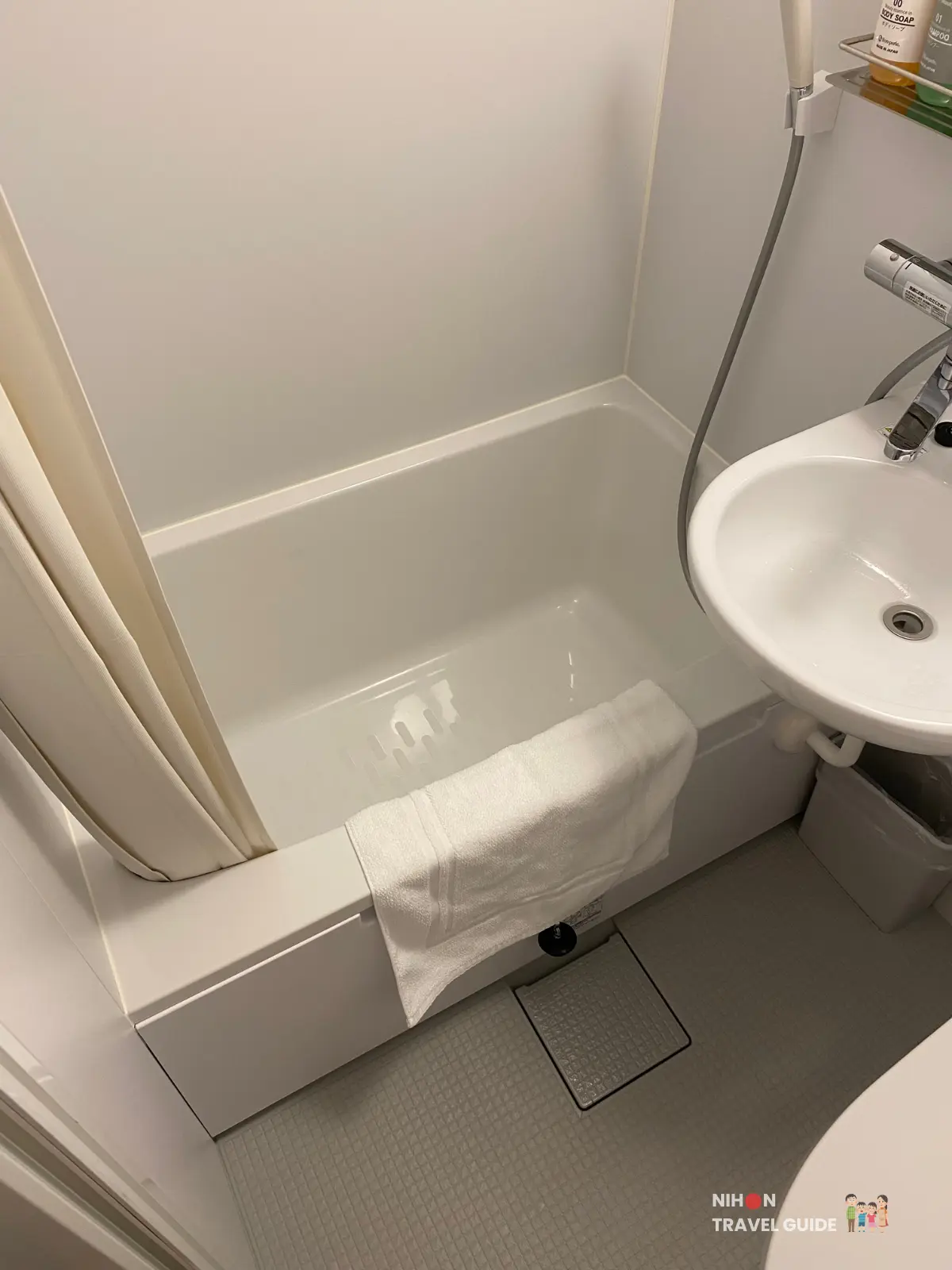 White unit bath at Hotel R9 The Yard Tsukuba with bathtub, showerhead, and floor towel.