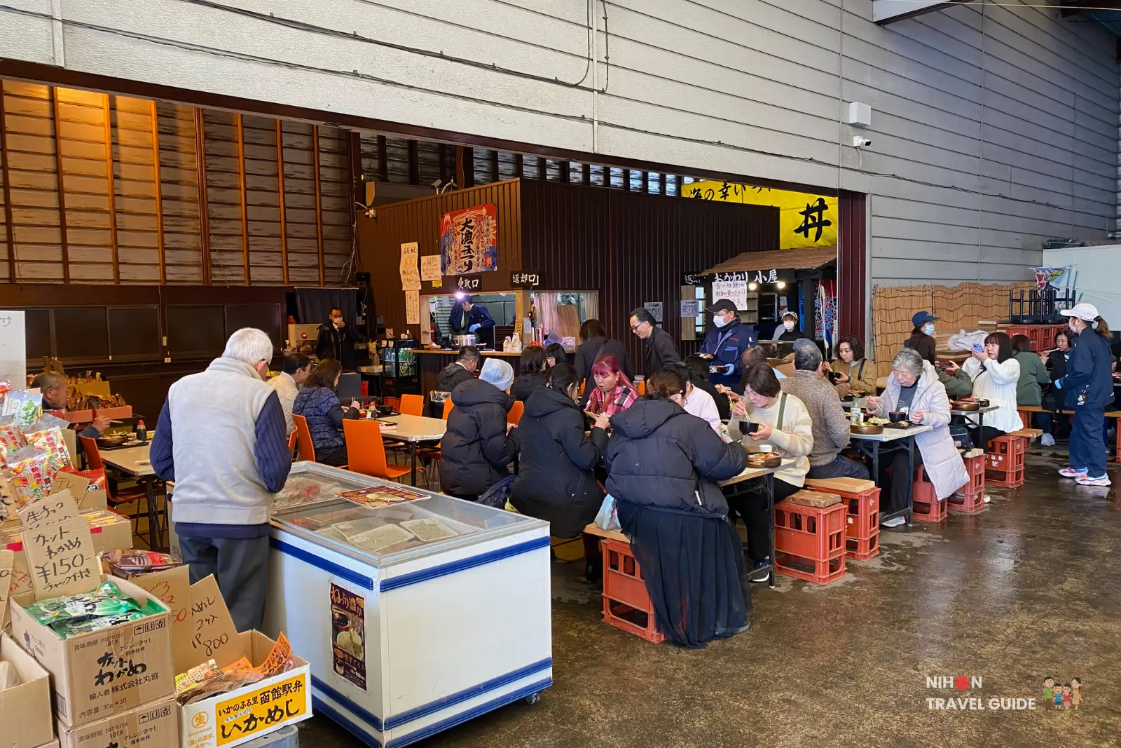 Packed communal dining area inside Tsuchiura Fish Market canteen with locals enjoying fresh fish meals at orange-crate tables, busy lunch scene in February 2026