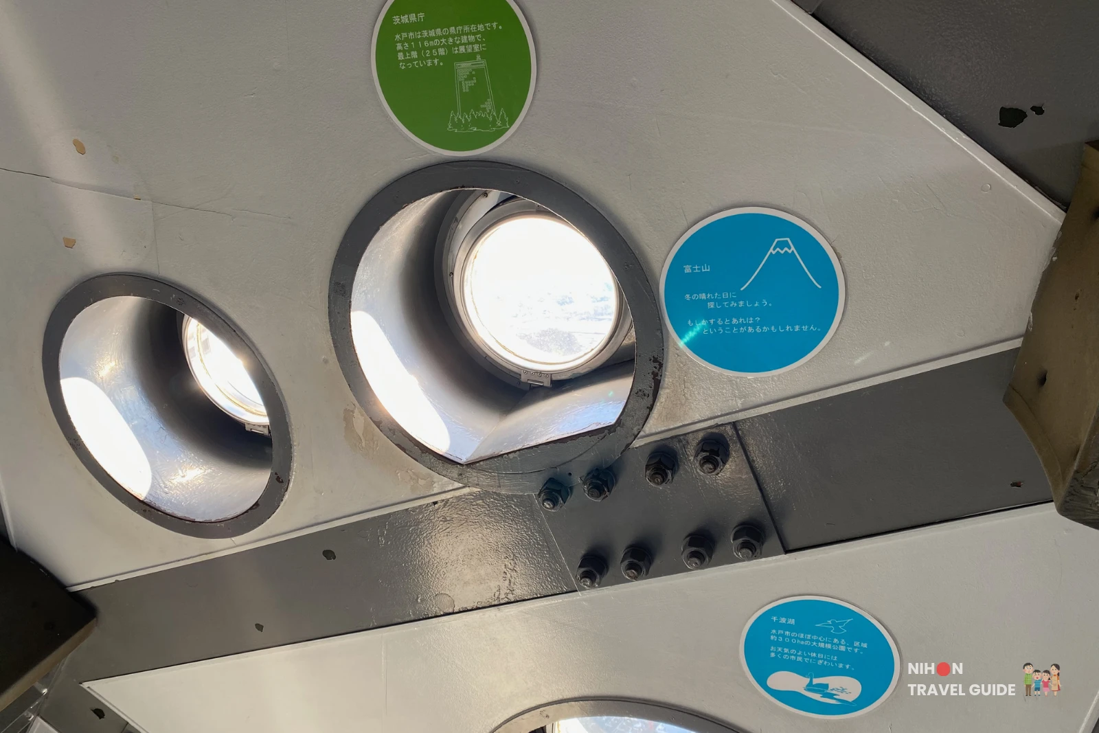 Landmark identification plaques on the Art Tower Mito observation deck showing three circular guides: a green plaque for the Ibaraki Prefectural Government building (116 metres tall), a blue plaque for Mount Fuji (visible on clear winter days), and a blue plaque for Lake Senba (a 300,000 m² park near the centre of Mito City), Ibaraki, Japan