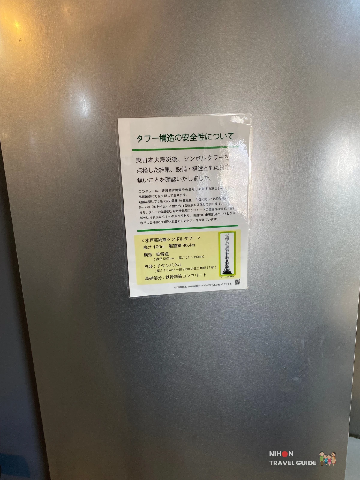 Structural safety notice posted on the steel wall of the Art Tower Mito observation deck, stating that after the 2011 Great East Japan Earthquake the tower was inspected and confirmed to have no damage to its equipment or structure, with technical specifications listing the tower height as 100m, observation deck at 86.4m, steel pipe construction, 57 titanium exterior panels, and reinforced concrete foundations, Mito City, Ibaraki, Japan