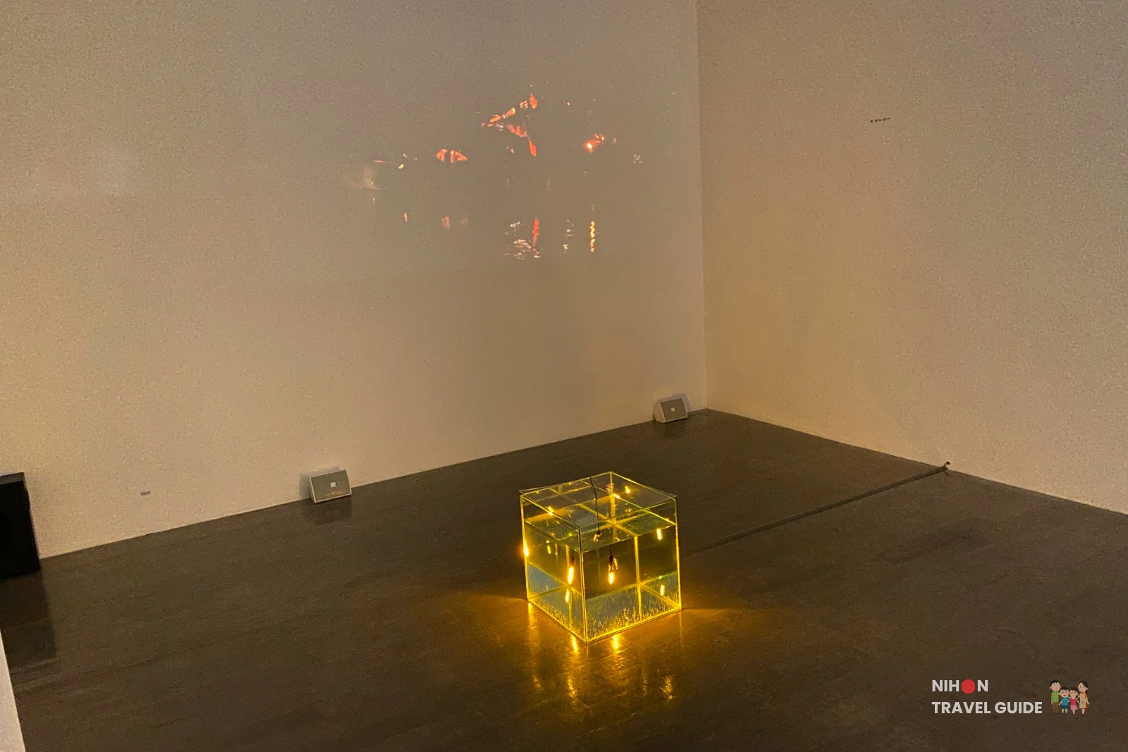 Illuminated yellow glass cube art installation glowing on the floor in the CRITERIUM 102 exhibition by Takuto Shiromaru at Art Tower Mito, with light projection on the wall