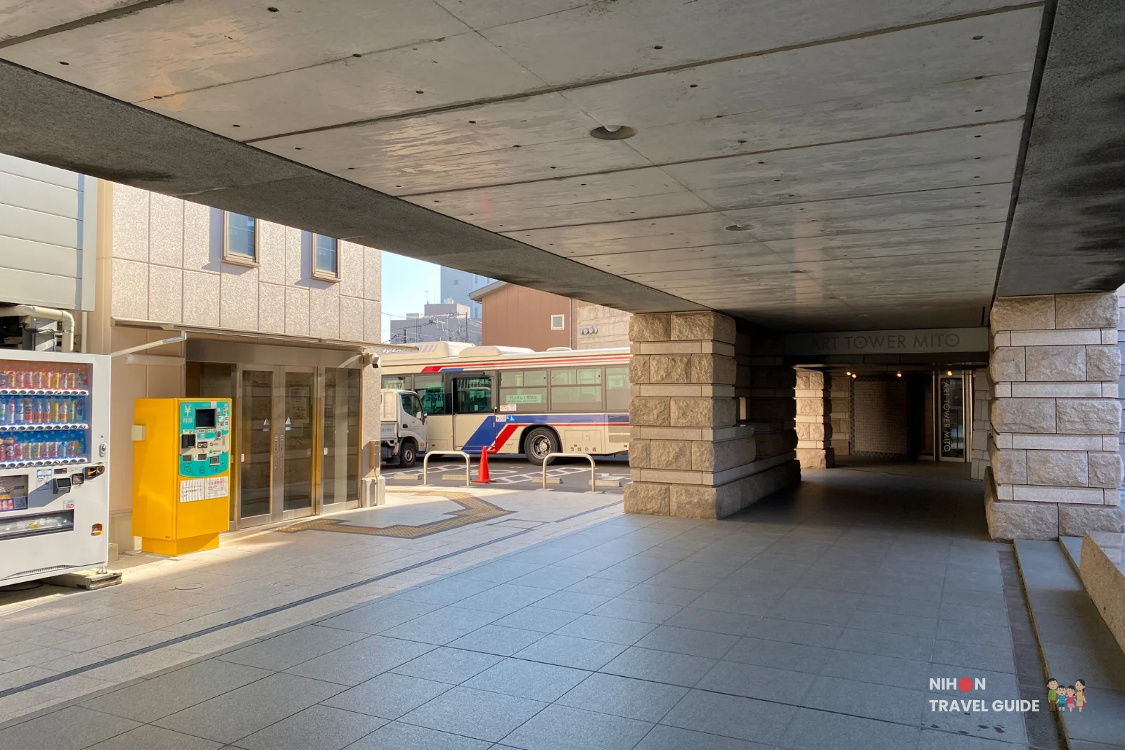 Covered walkway entrance of the Gokencho Parking Building adjacent to Art Tower Mito, with vending machines and a local bus visible outside, Mito City, Ibaraki, Japan