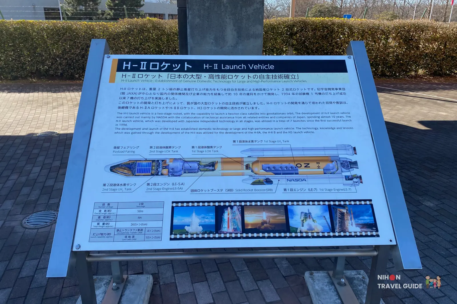 Close-up of the outdoor H-II Launch Vehicle information board at JAXA Tsukuba Space Center, showing a diagram of the rocket stages and launch photos.