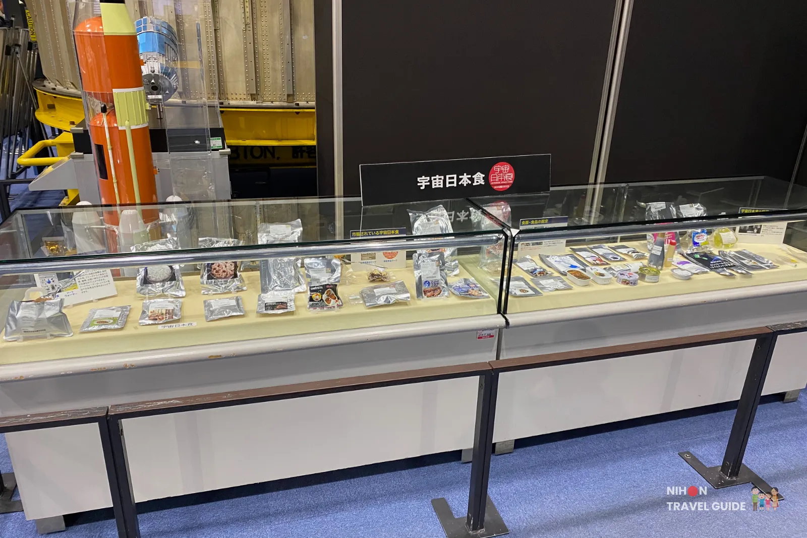 Glass display case at JAXA Tsukuba Space Center showing a variety of packaged Japanese space foods eaten by astronauts.