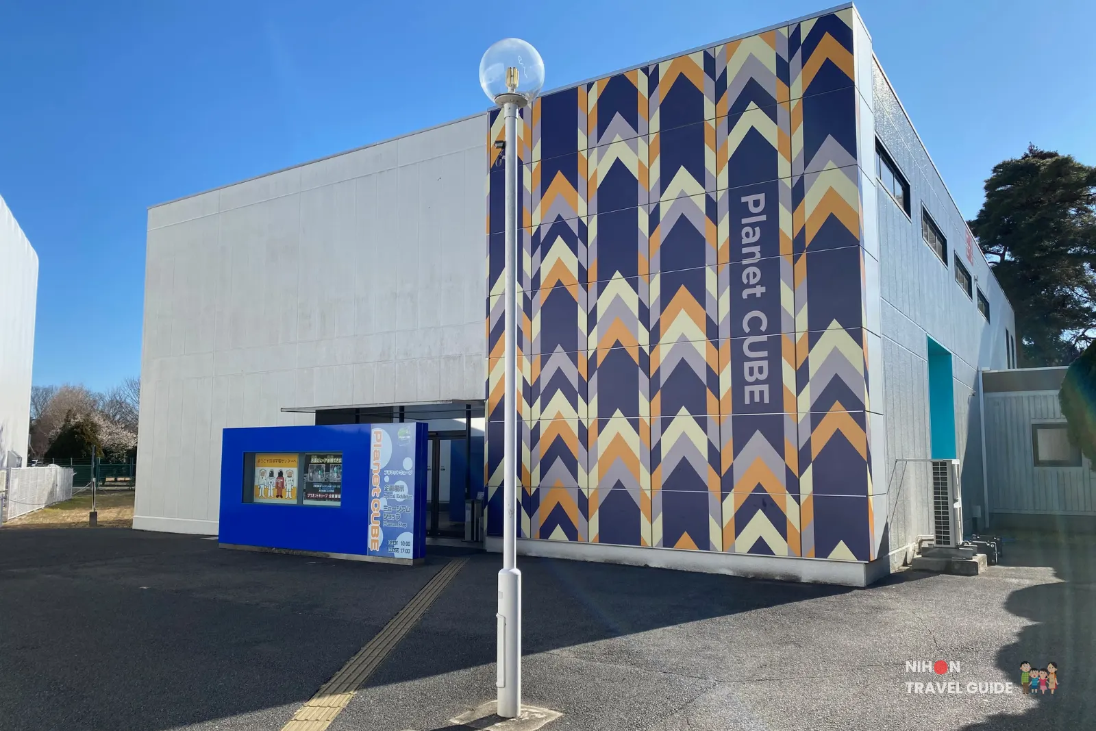 Exterior of the Planet Cube gift shop building at JAXA Tsukuba Space Center featuring a colourful geometric facade and entrance under a blue sky.
