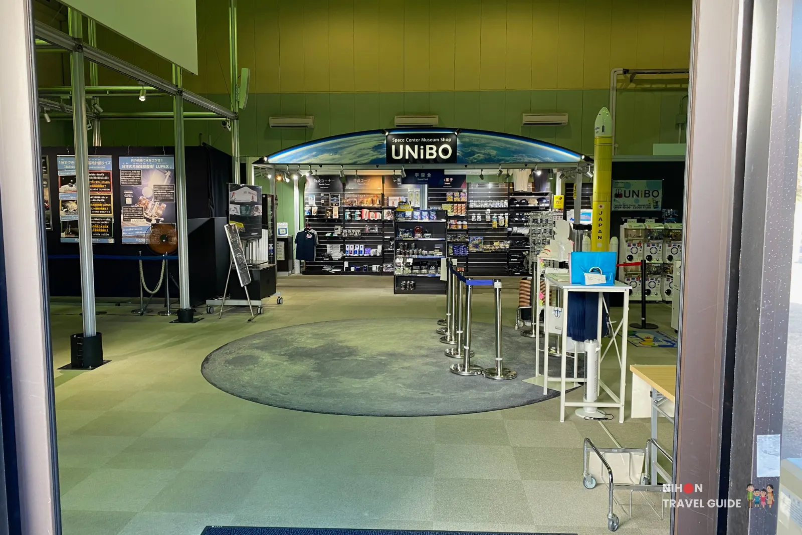 View from the doorway into the Planet Cube gift shop at JAXA Tsukuba Space Center, showing the UNiBO museum shop sign and displays of space merchandise inside.