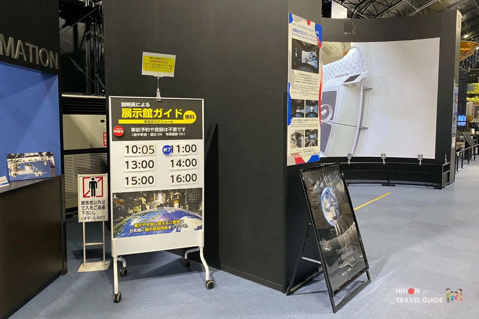 jaxa-tsukuba-space-dome-free-guided-tour-schedule-sign Schedule board inside the JAXA Tsukuba Space Dome showing times for the free exhibition hall guided tours beside a large curved video screen.