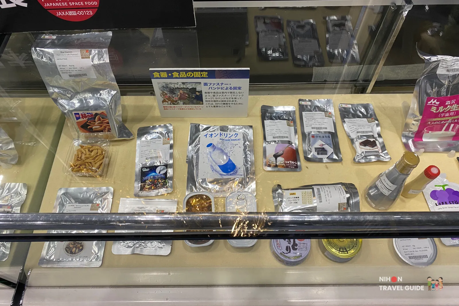 Detailed view of Japanese space food samples such as snacks, Pocari Sweat drink pouch and canned dishes in a glass case at JAXA Tsukuba Space Center.