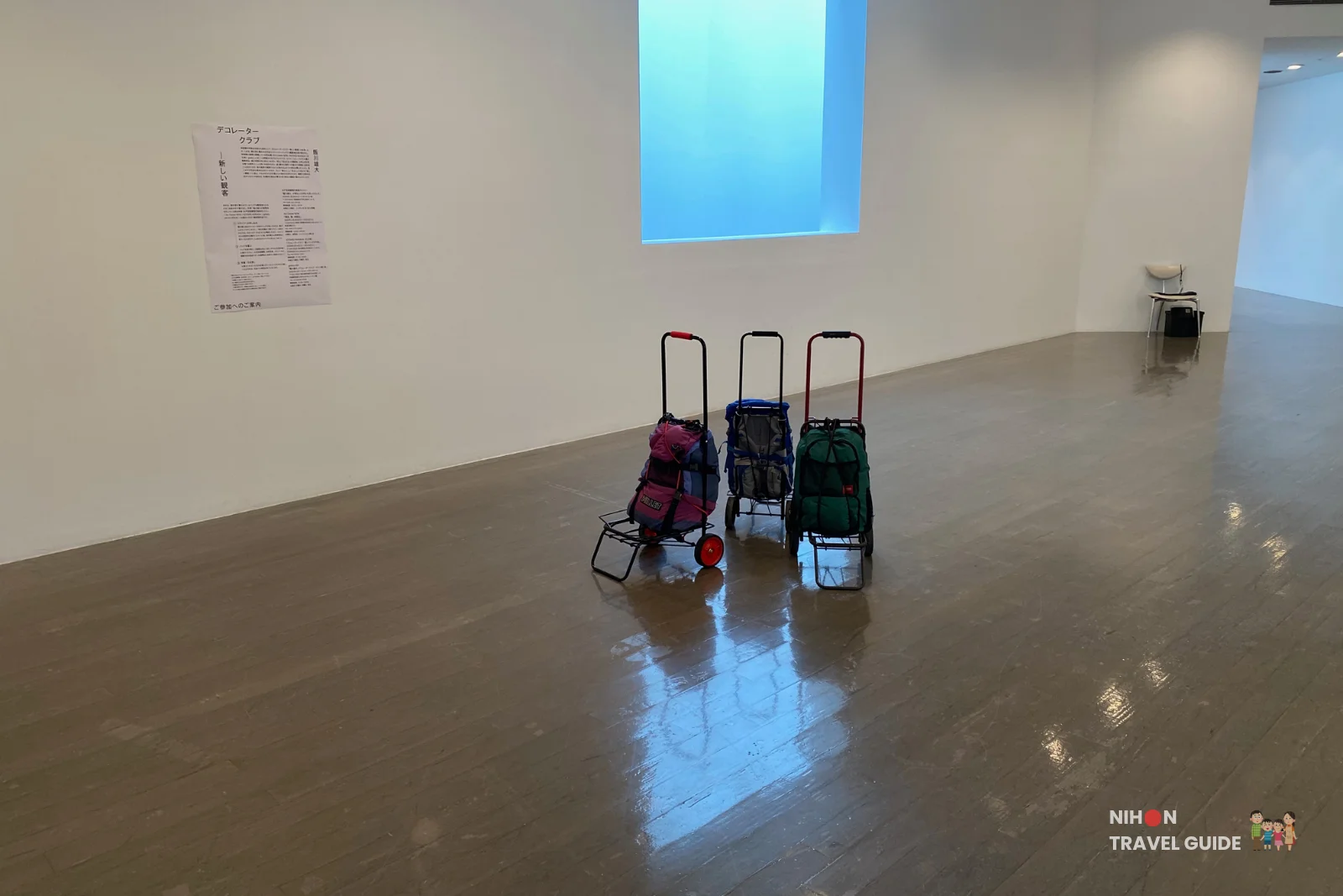 Three colorful luggage carts with backpacks lined up in the gallery for Takehiro Iikawa’s participatory “Decorator Crab — Make Space, Use Space” installation.