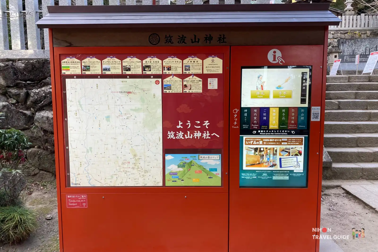 Red information kiosk at Tsukubasan Shrine with area maps, shrine guidance, and touchscreen panel beside stone steps.