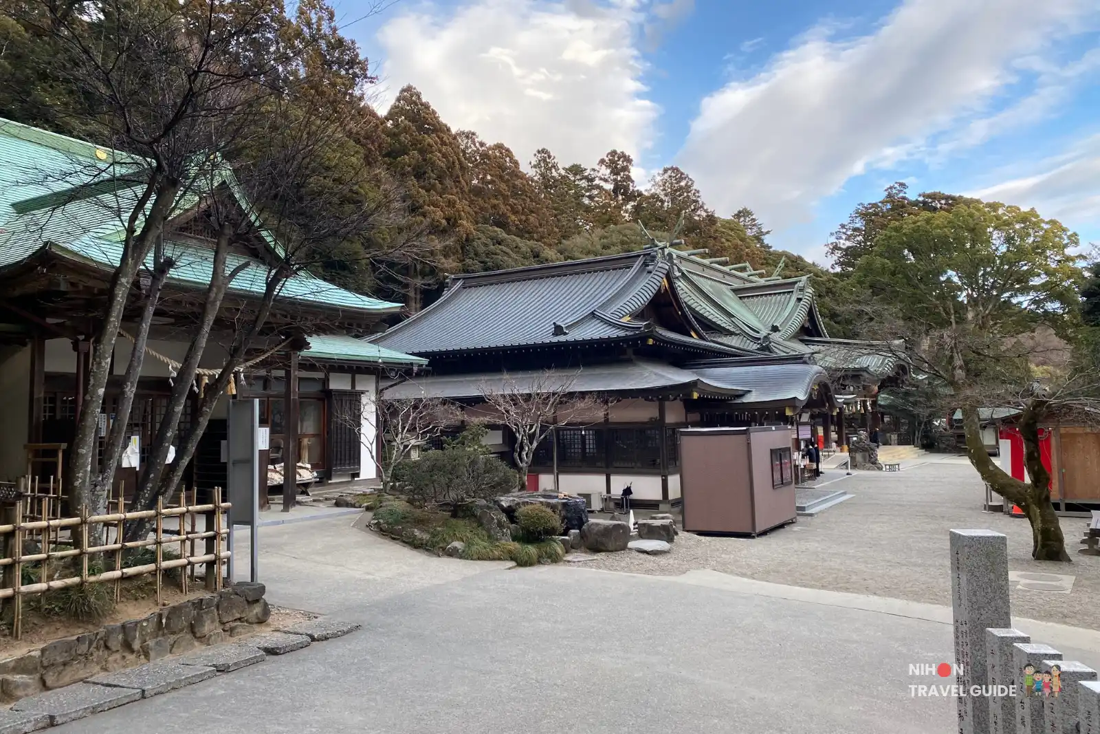 Courtyard view of Tsukubasan Shrine showing the shrine office building beside the main worship hall and surrounding forested hillside.