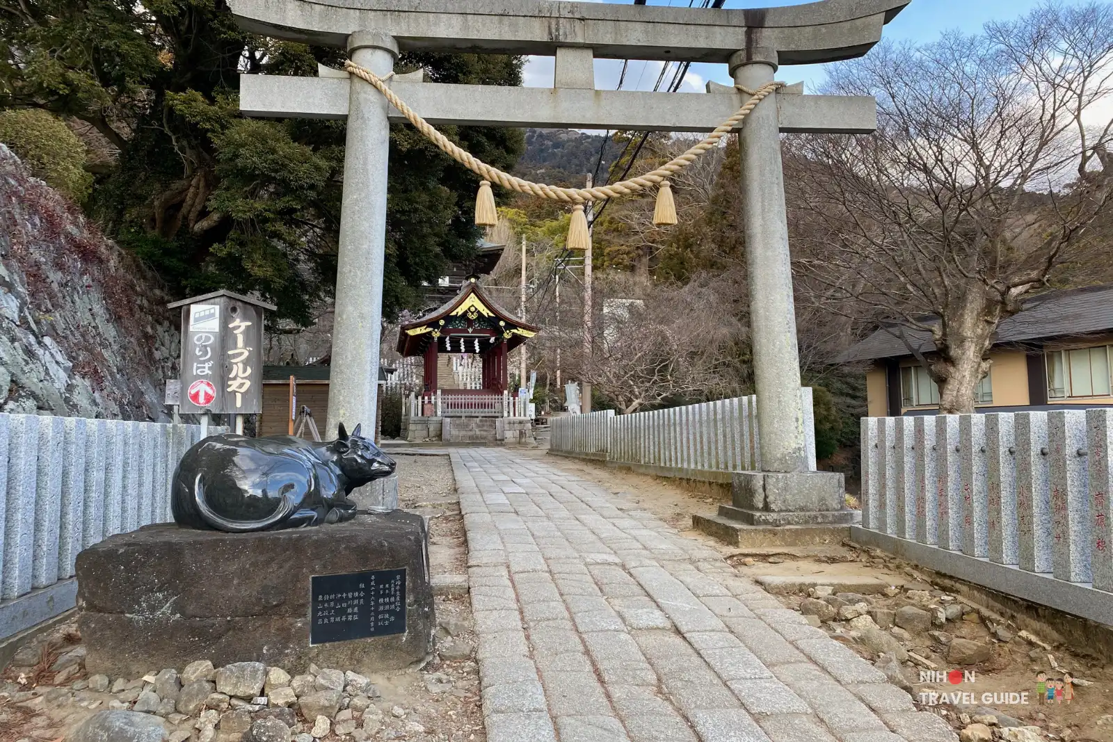 Stone second torii gate at Tsukubasan Shrine with black cow statue and ropeway sign on the approach path.