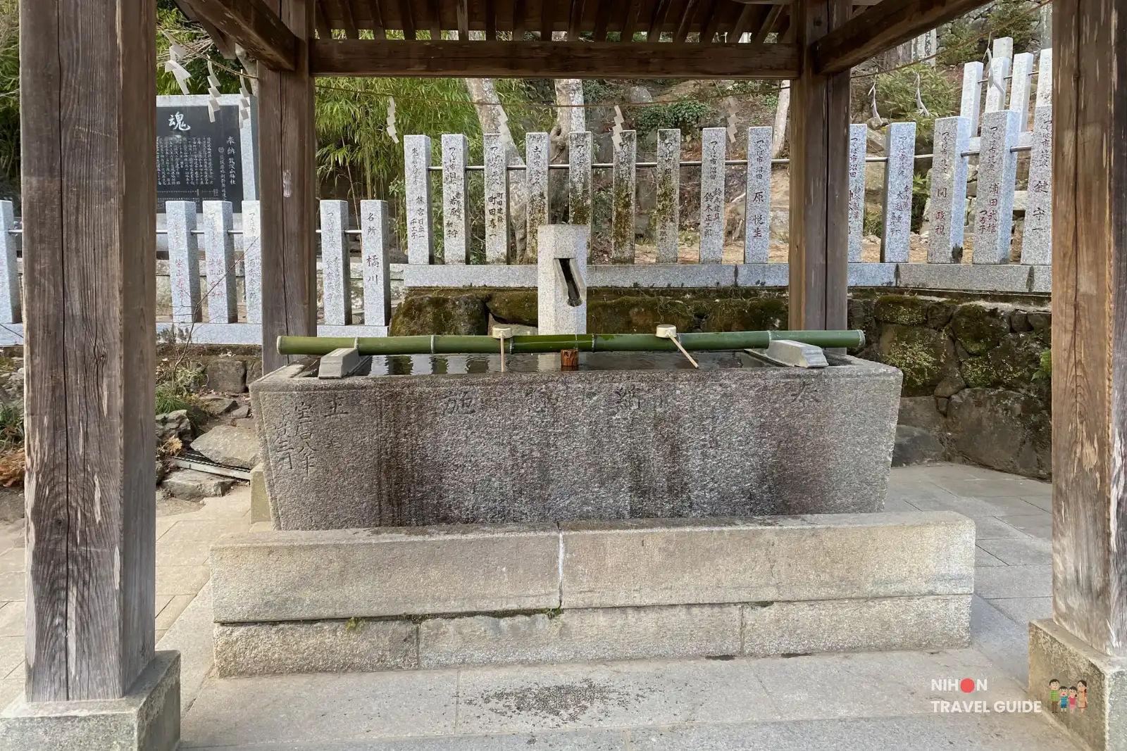 Stone water basin under a wooden roof at the temizuya where visitors purify hands and mouth before worship.