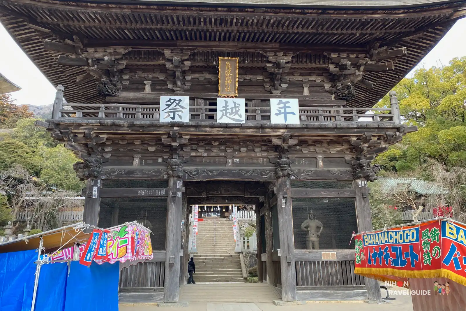 Large two-story wooden Zuishinmon gate with guardian figures, standing before the stone stairway to Tsukubasan Shrine.