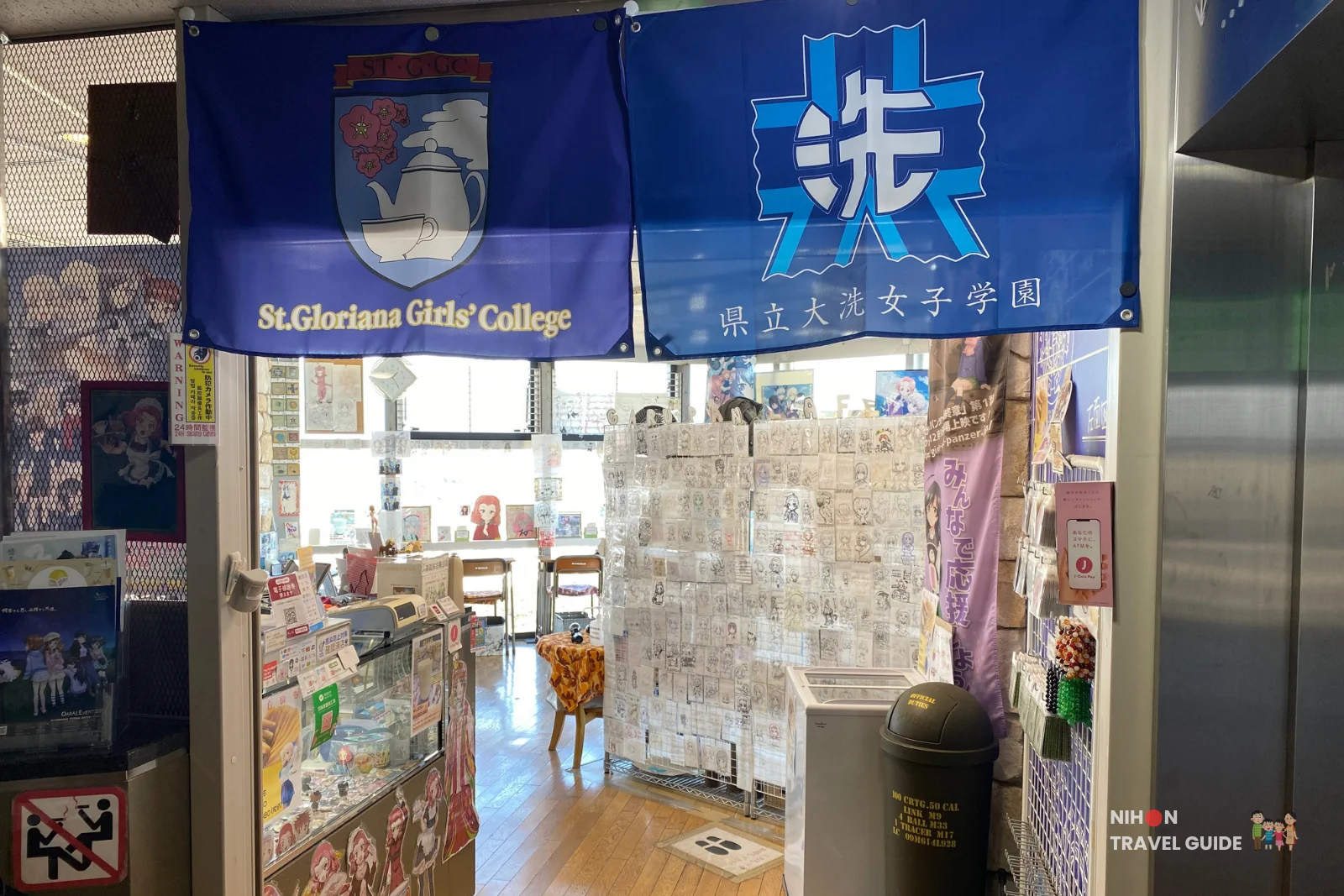 Entrance to Café Panzer Vor on the second floor of Oarai Marine Tower, featuring large blue banners of St. Gloriana Girls’ College and 県立大洗女子学園 (Oarai Girls Academy), with the fan art wall visible inside, Ibaraki, Japan