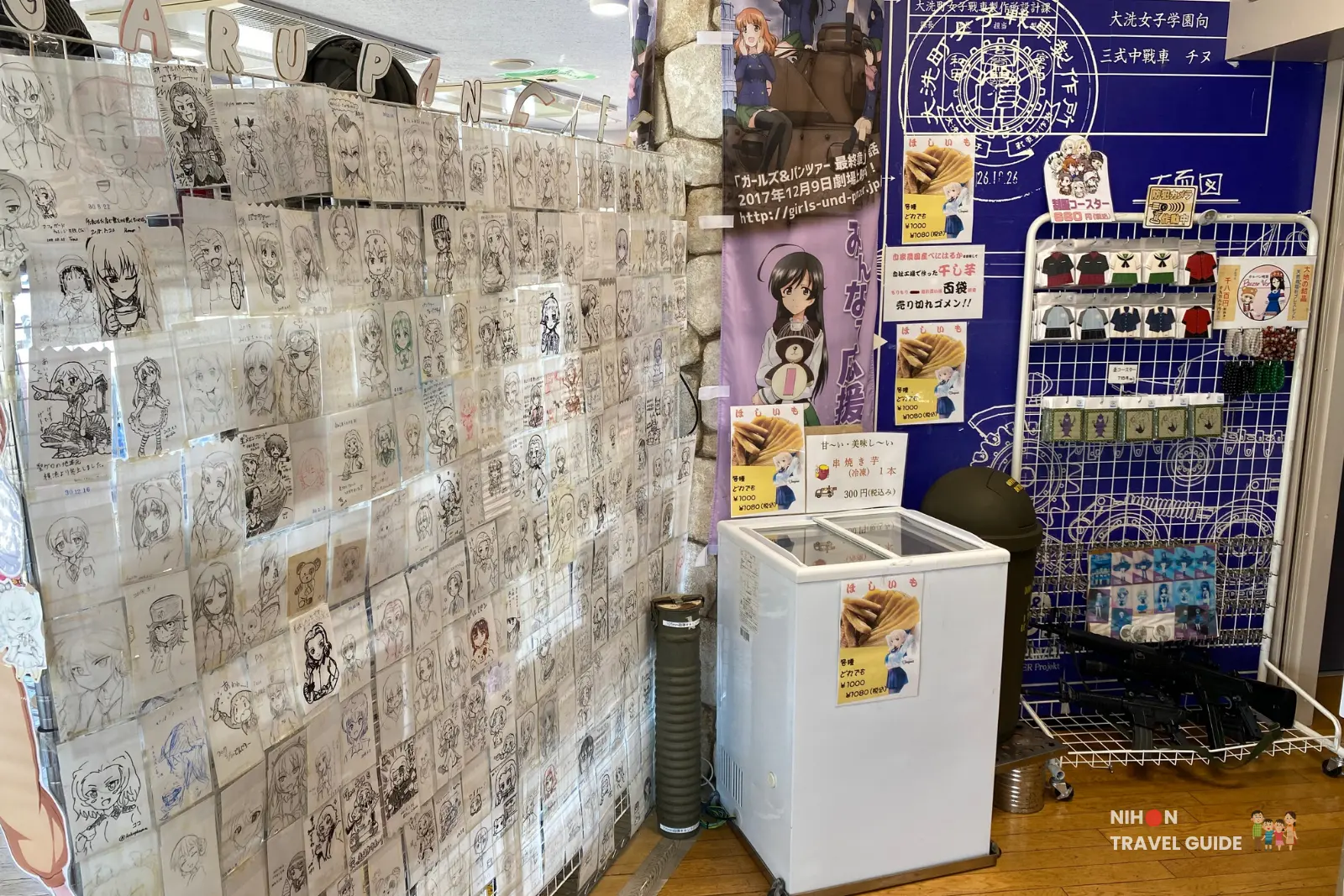 Fan art wall covered with hundreds of hand-drawn Girls und Panzer sketches at Café Panzer Vor on the second floor of Oarai Marine Tower, with imomo (sweet potato) snacks for sale, a small freezer, and themed merchandise, Ibaraki, Japan
