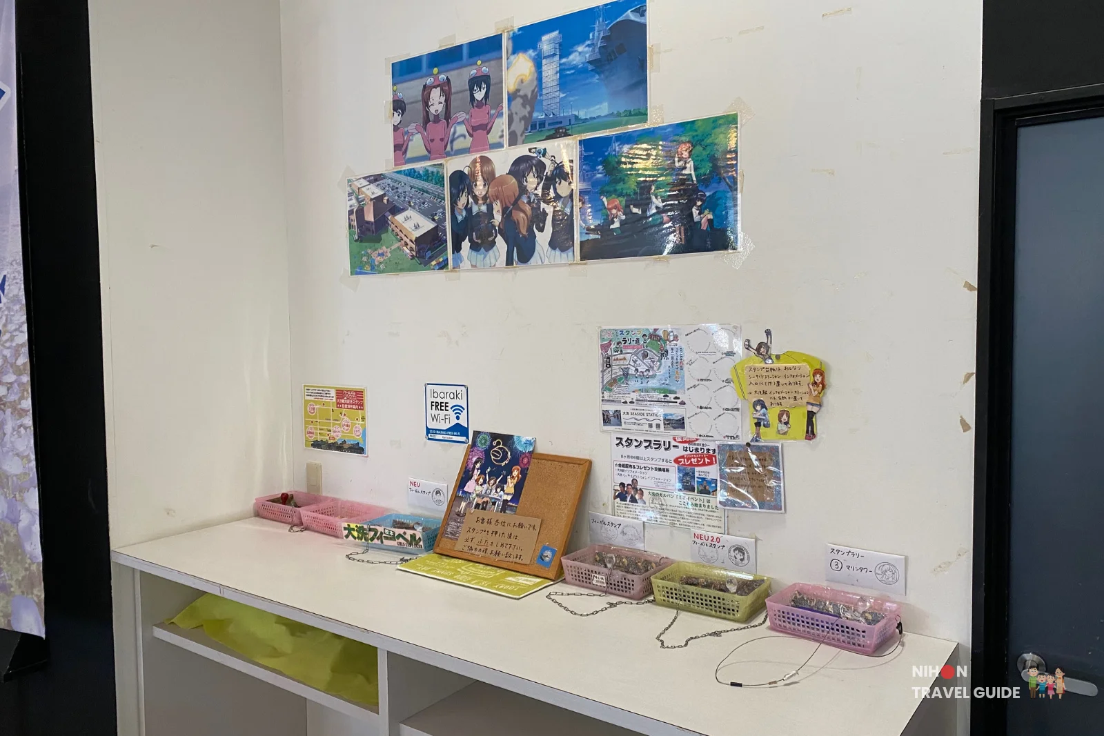 Girls und Panzer anime corner at Oarai Marine Tower with character posters, stamp rally information, and a white counter with stamp pads and baskets, Ibaraki Prefecture, Japan