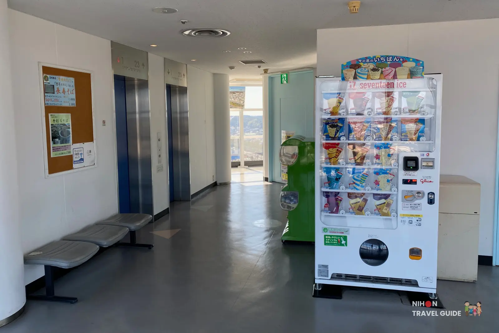 oarai-marine-tower-observation-deck-lobby-vending-machines Observation deck lobby at Oarai Marine Tower with elevator banks, grey waiting seats, a large Seventeen Ice cream vending machine, and a green gashapon capsule machine, offering a view of the town through the windows in the background, Ibaraki Prefecture, Japan