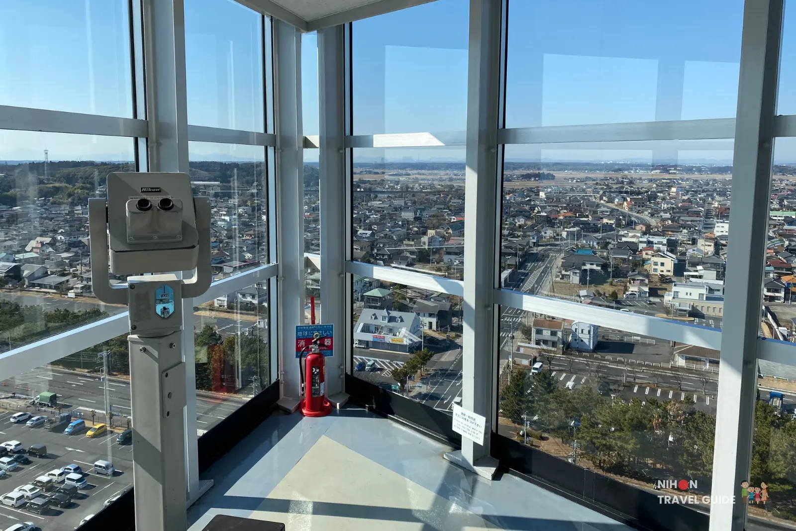 Nikon binoculars on the observation deck of Oarai Marine Tower framing the southwest inland view over Oarai town, roads, and surrounding countryside on a bright clear day, Ibaraki Prefecture, Japan