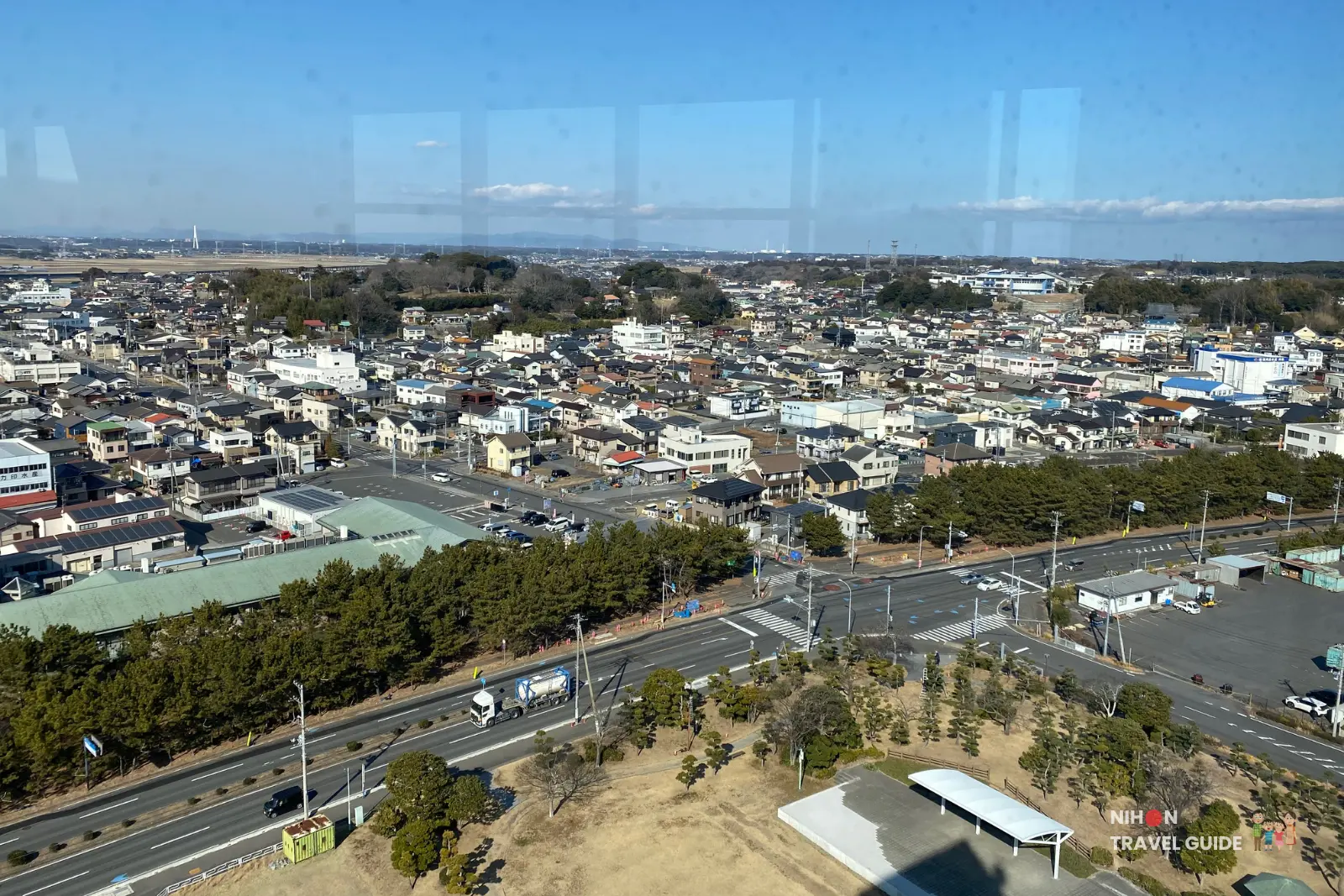 Sweeping southwest panorama from Oarai Marine Tower observation deck capturing the spread of Oarai town, busy roads with vehicles, commercial buildings, and forested hills in the background, Ibaraki Prefecture, Japan