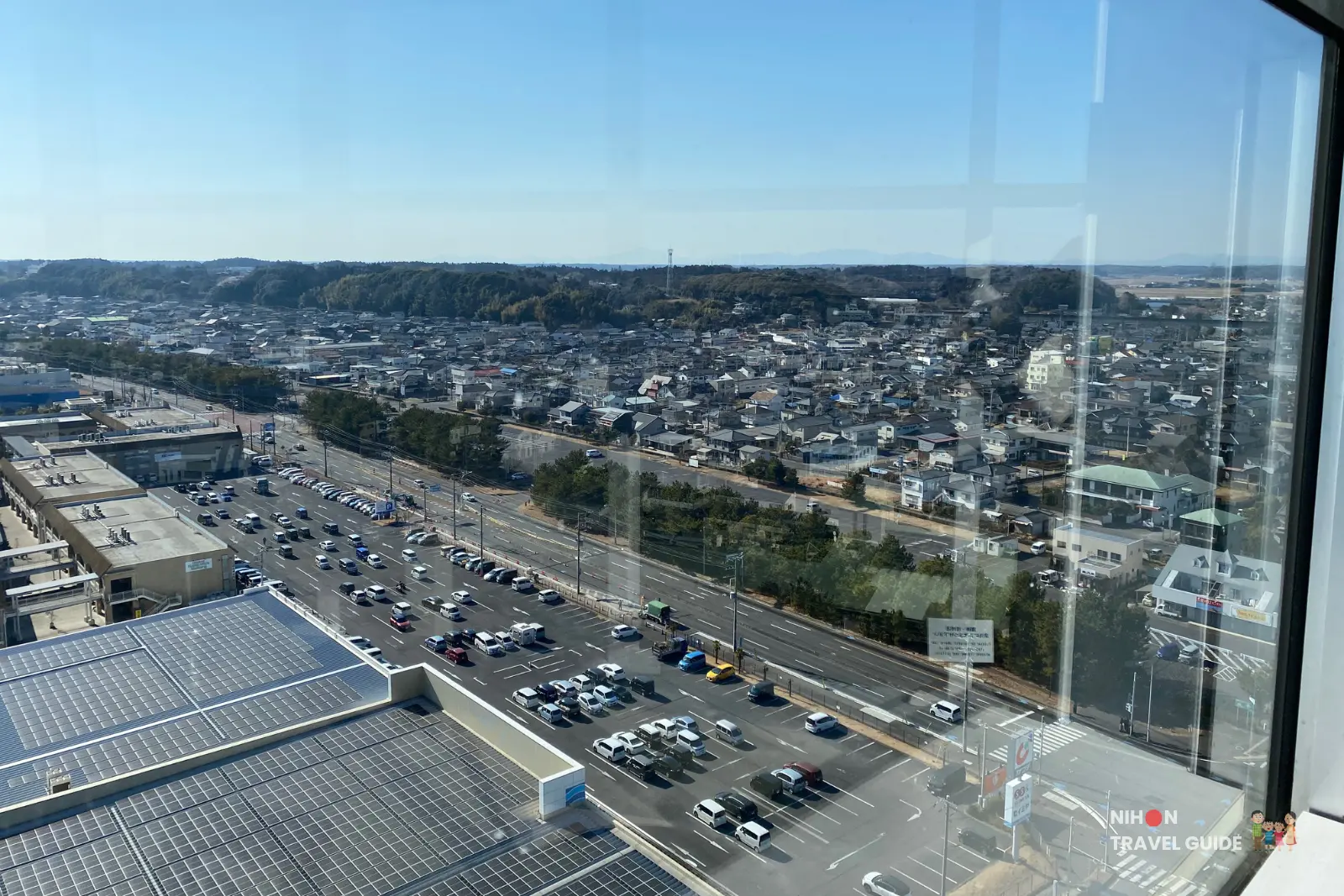 Southwest view from Oarai Marine Tower showing a large building with solar panels, extensive parking lots, and the sprawling town stretching toward distant mountains, Ibaraki, Japan