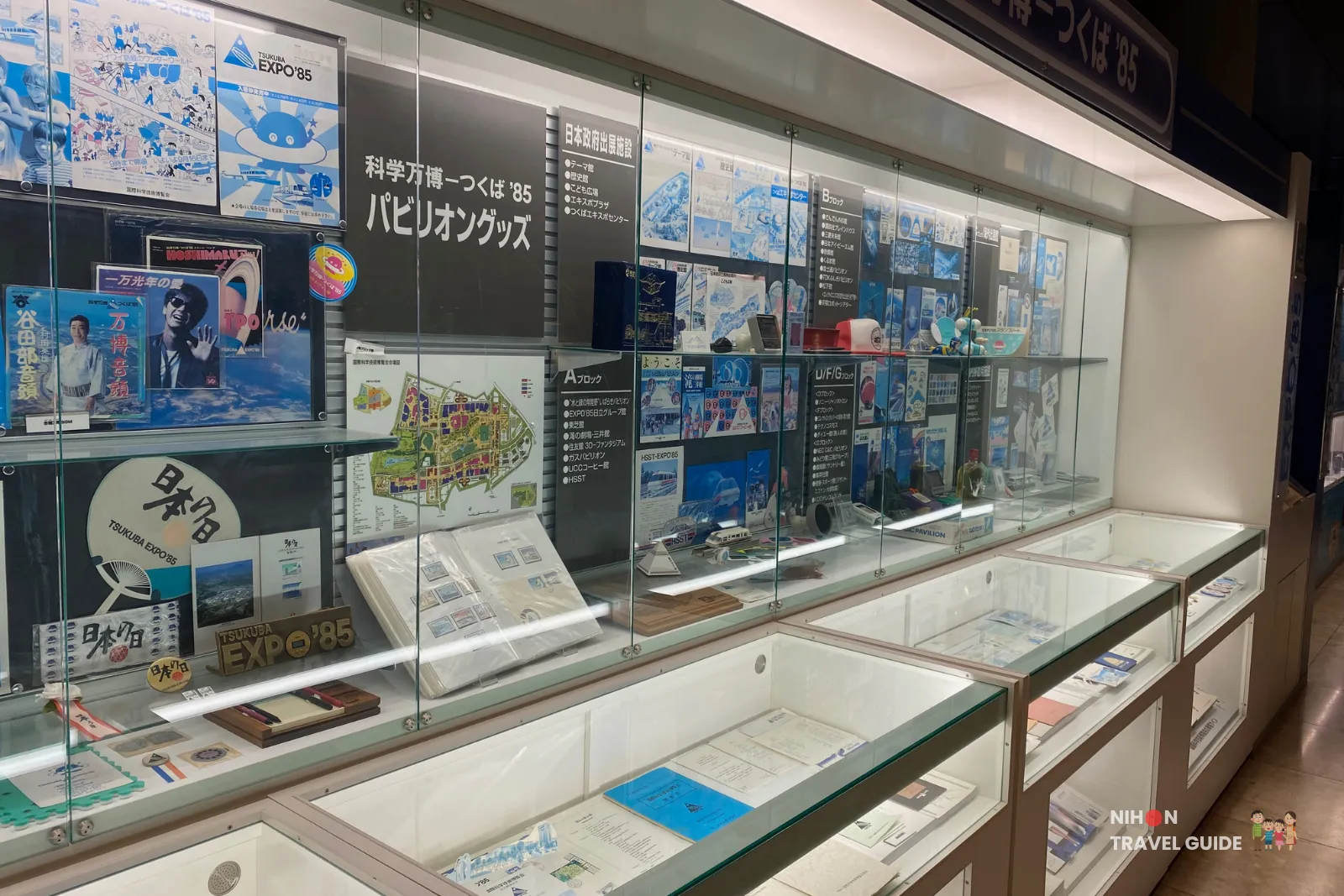Long glass display case in the Tsukuba Expo '85 Memorial showing pamphlets, maps, posters, and official goods from various pavilions of the 1985 Tsukuba Expo.